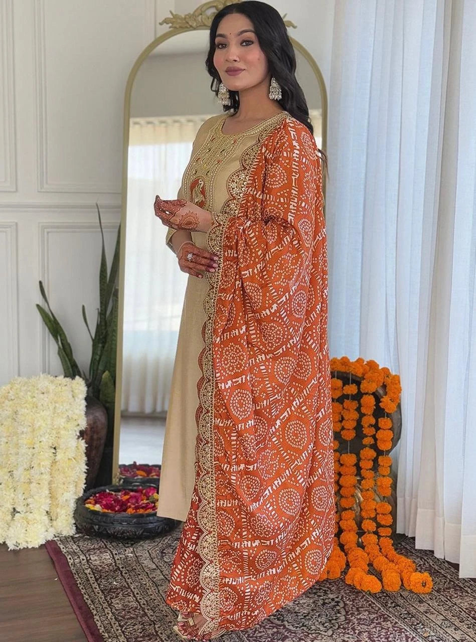 Woman in traditional outfit with orange and beige patterned dupatta standing in a decorated room.
