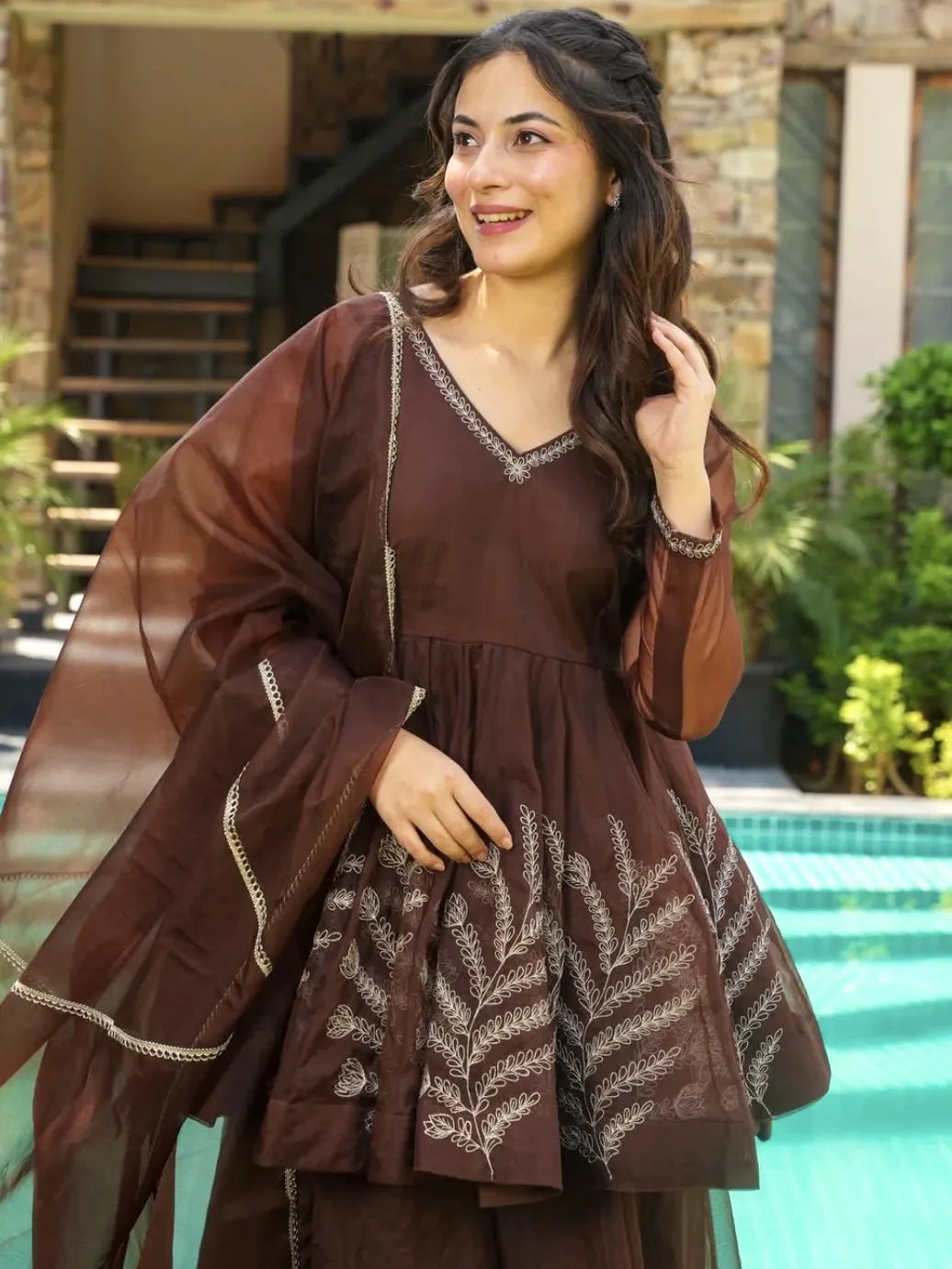 Woman in a brown dress with embroidery standing by a pool