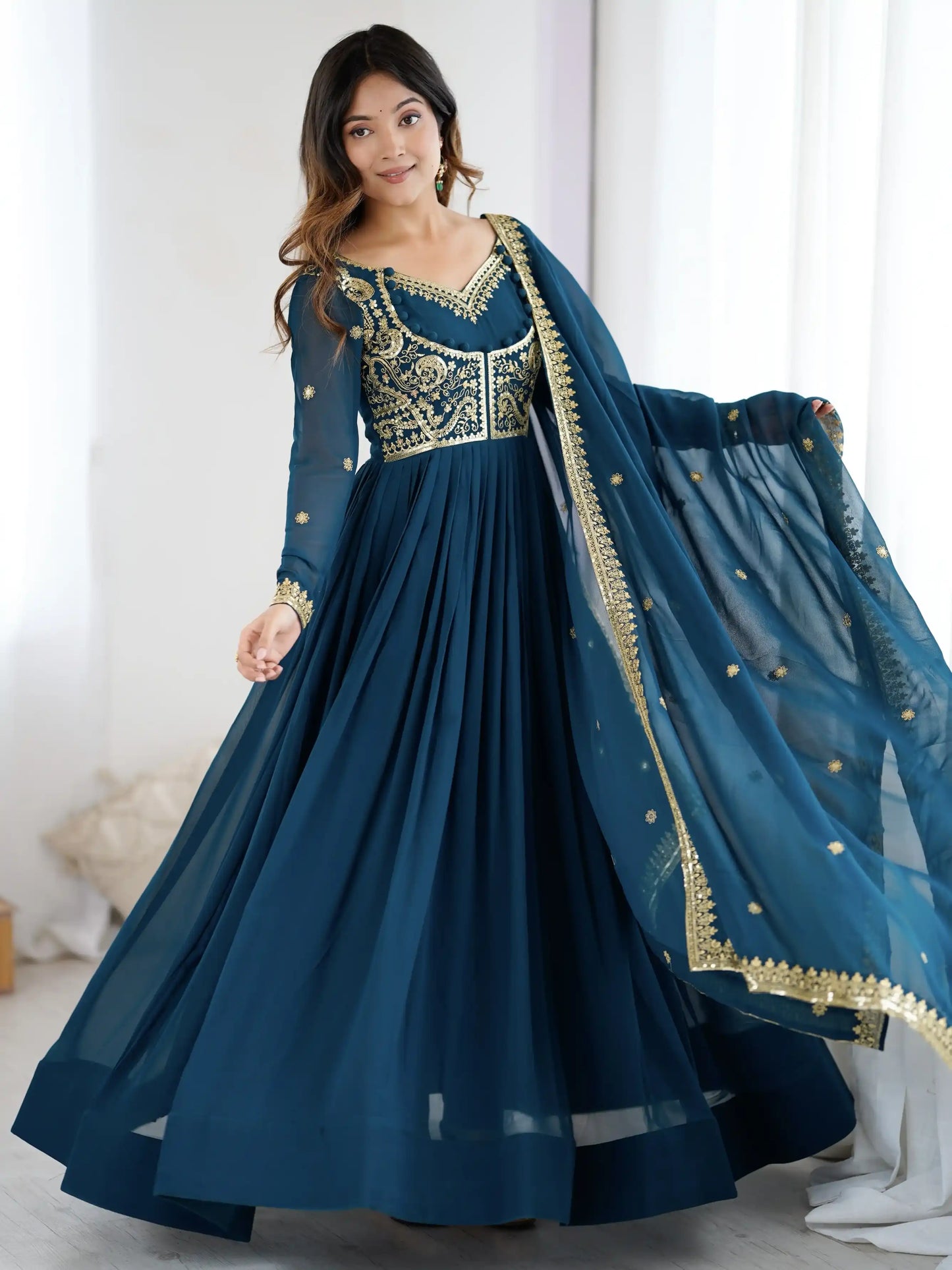 Woman wearing a blue traditional outfit with gold embroidery in a bright room.