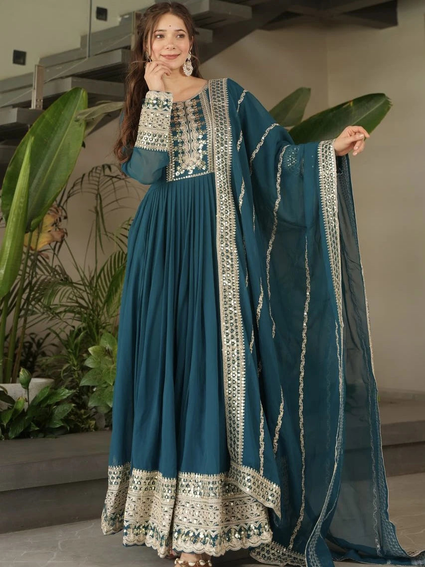 Woman wearing a teal traditional outfit with white embroidery indoors.