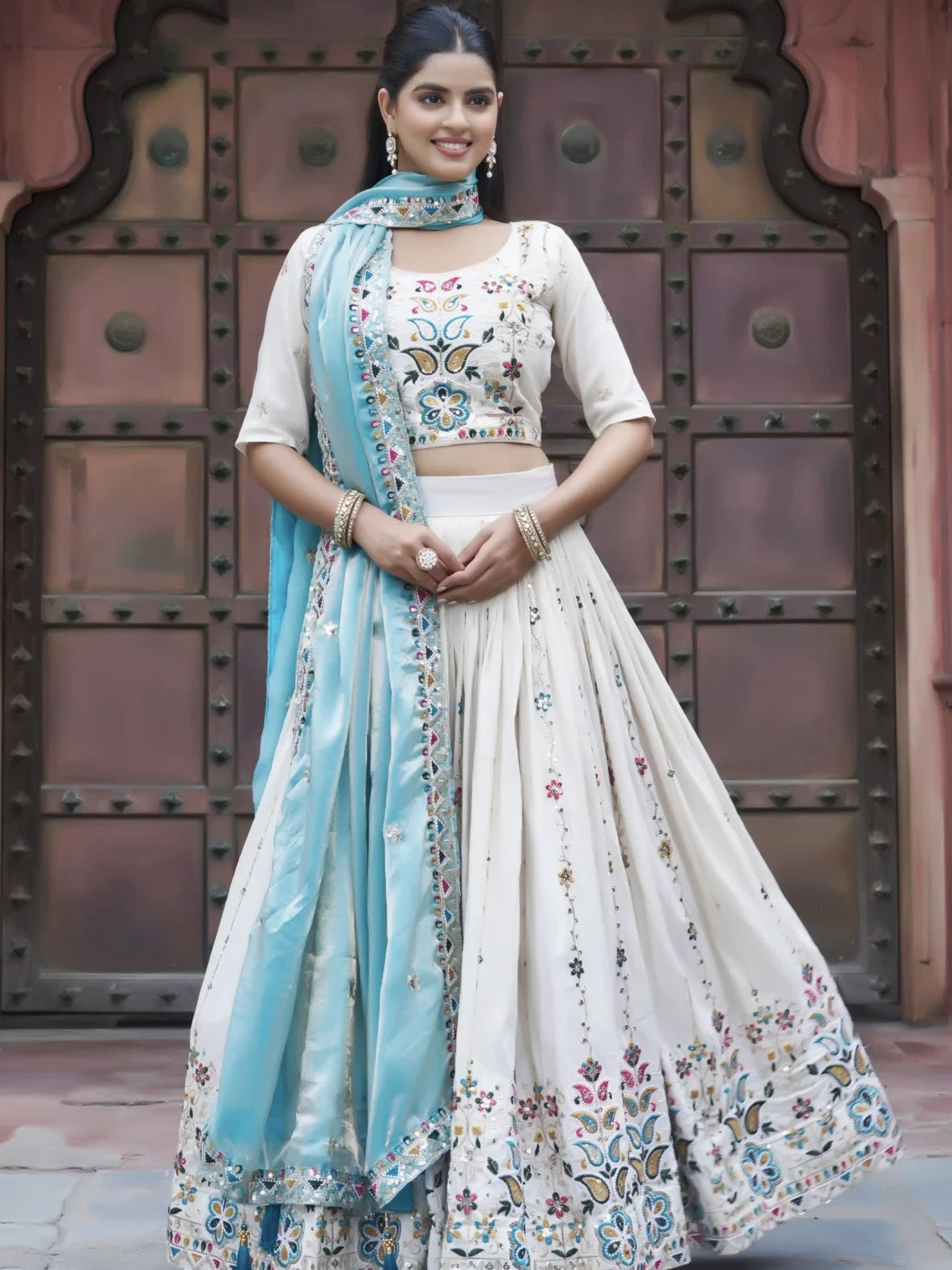 Woman in traditional outfit with floral patterns in front of a decorative door.