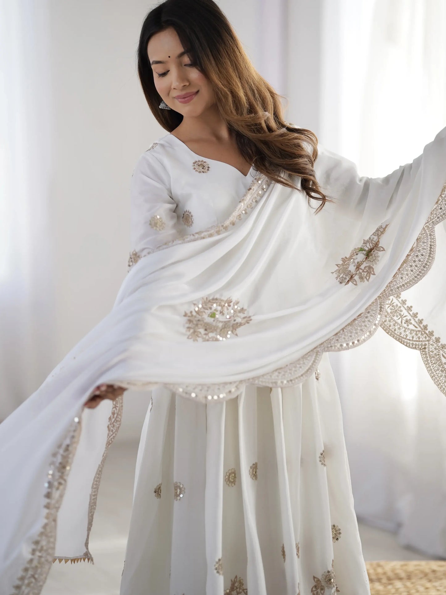 Woman wearing a white saree with gold embroidery against a white background