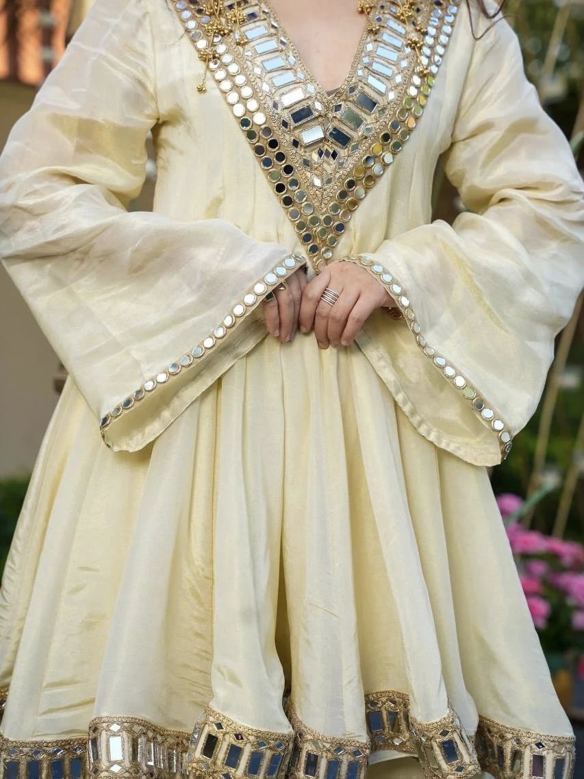 Cream-colored traditional outfit with intricate mirror work on a blurred natural background