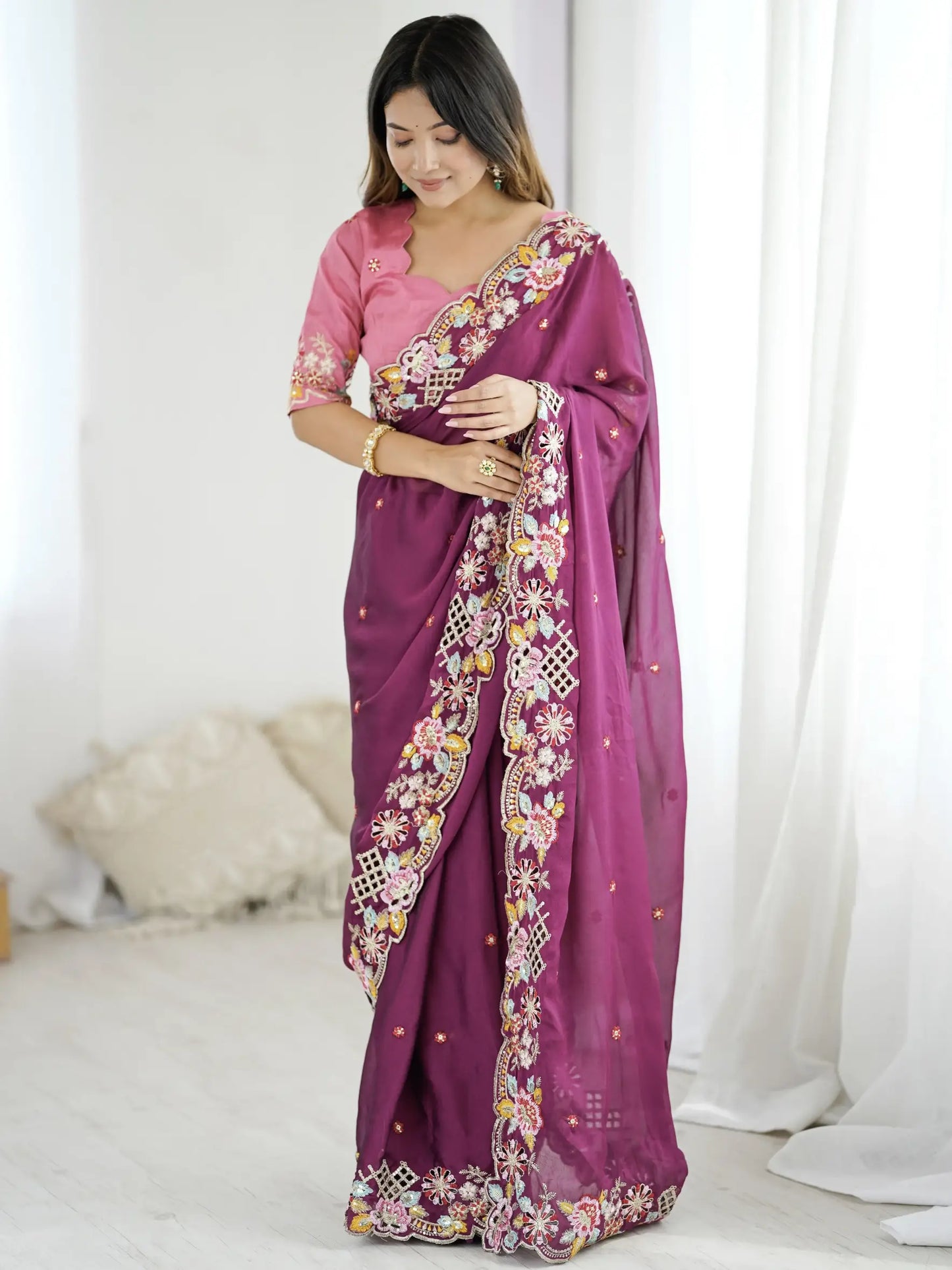 Woman wearing a purple saree with floral patterns in a bright room.