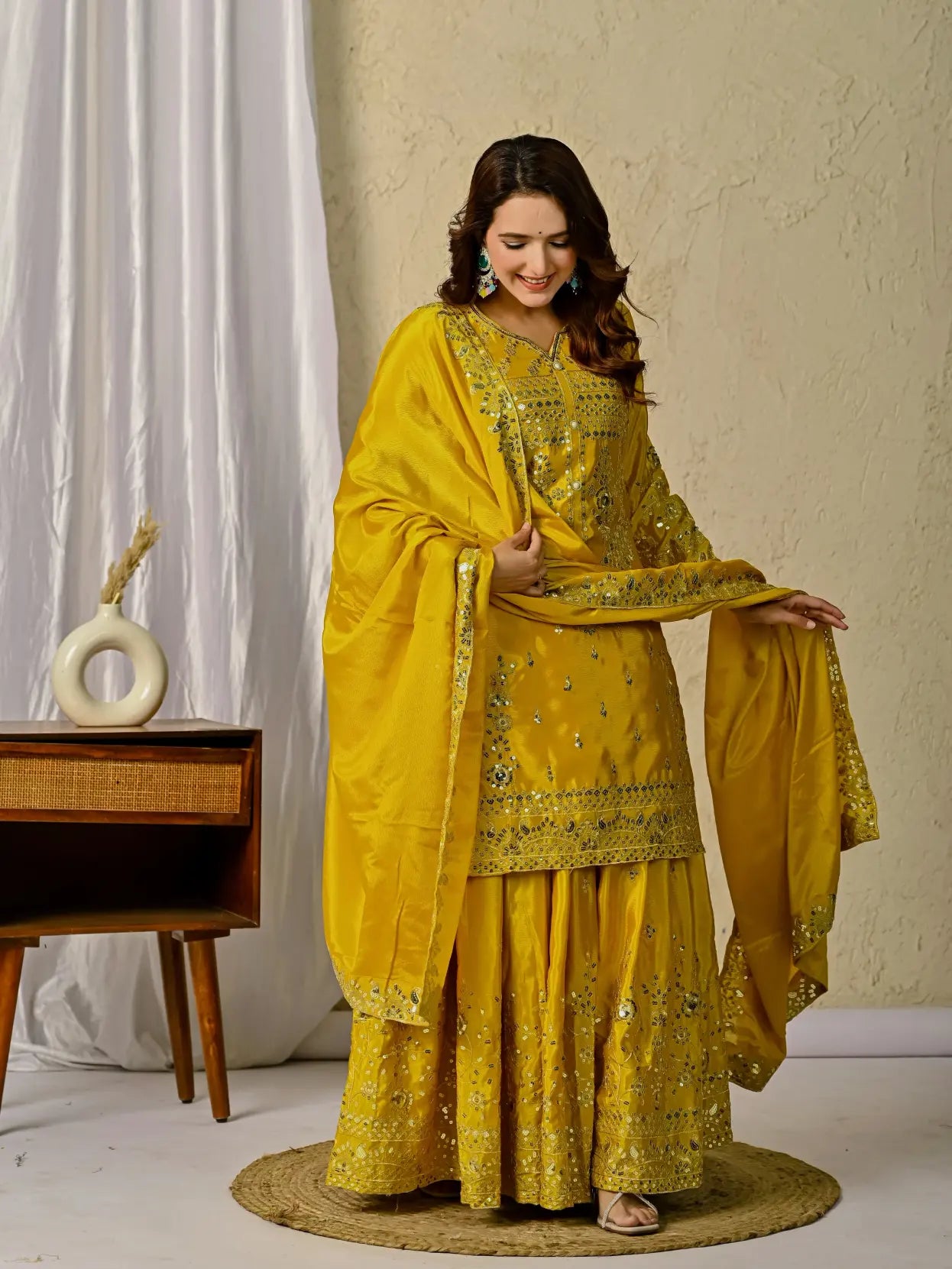 Woman in a yellow traditional outfit with embroidery, standing indoors against a neutral background.