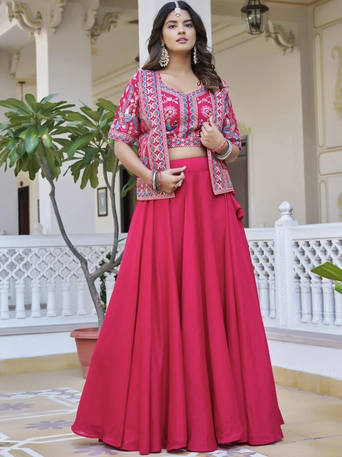 Woman in a pink traditional outfit with a patterned top in an elegant indoor setting.