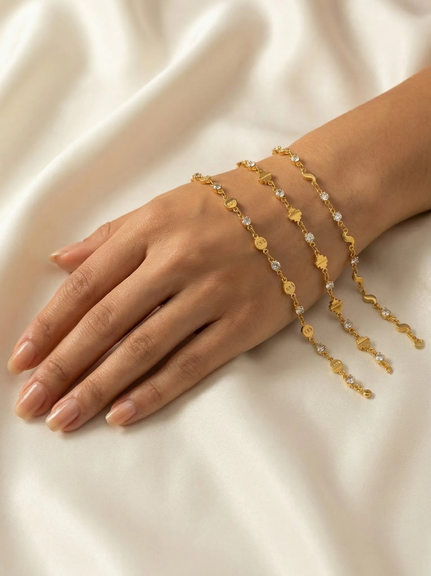 Gold bracelet with floral designs on a hand against a beige fabric background