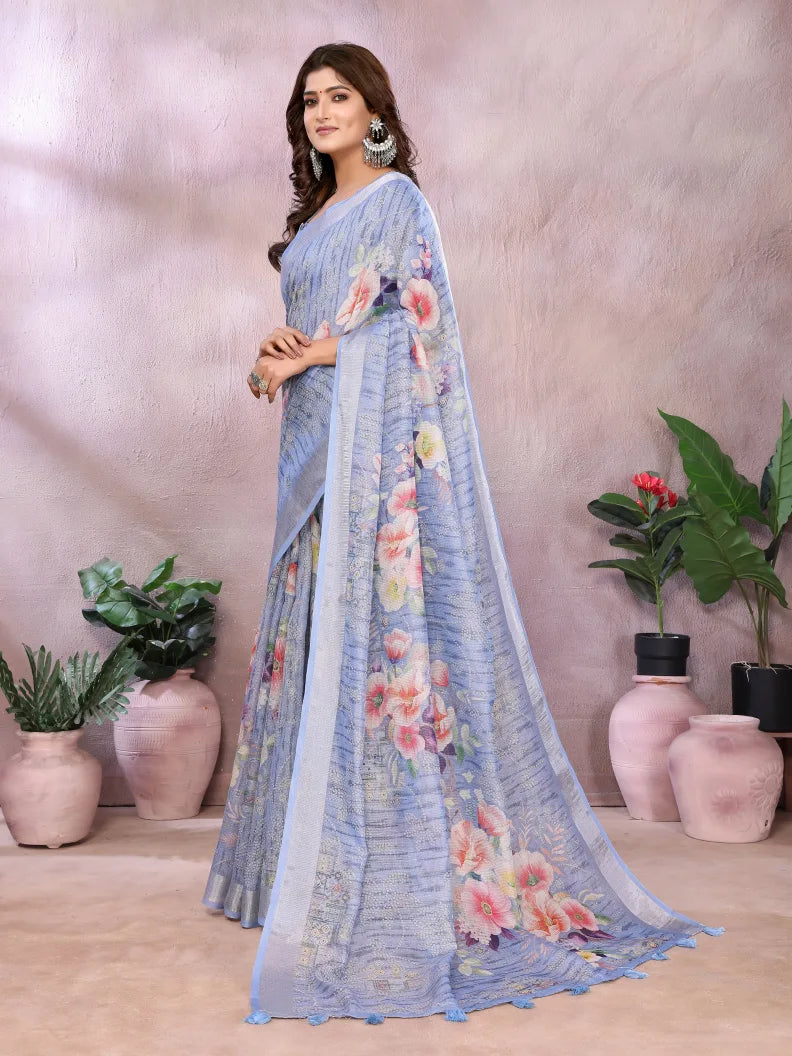 Woman wearing a light blue saree with floral patterns in a room with plants.