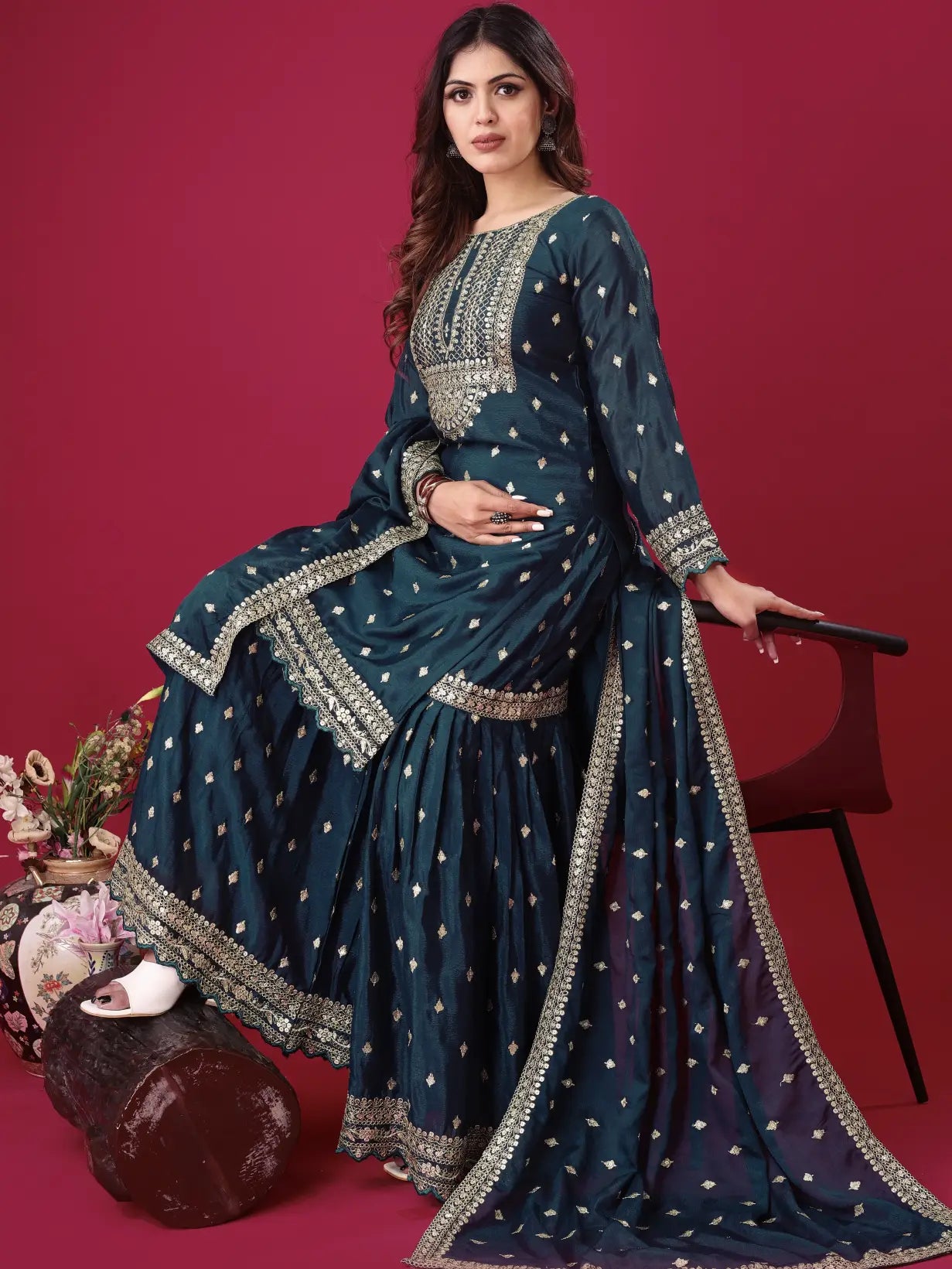 Woman in a traditional teal outfit with gold embroidery against a red background