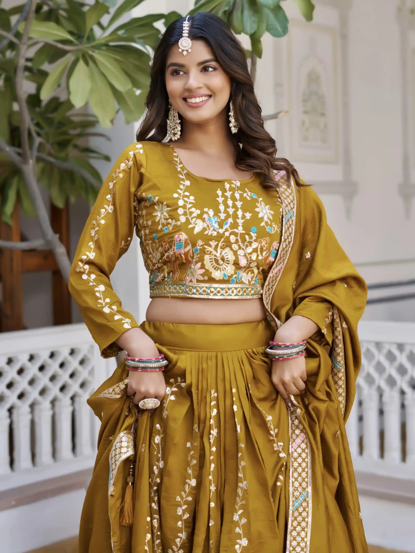 Woman in a traditional mustard yellow outfit with intricate designs, standing indoors.