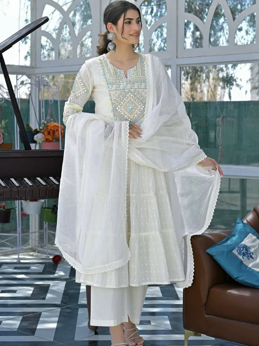 Woman in a white traditional outfit with intricate designs in a modern indoor setting.