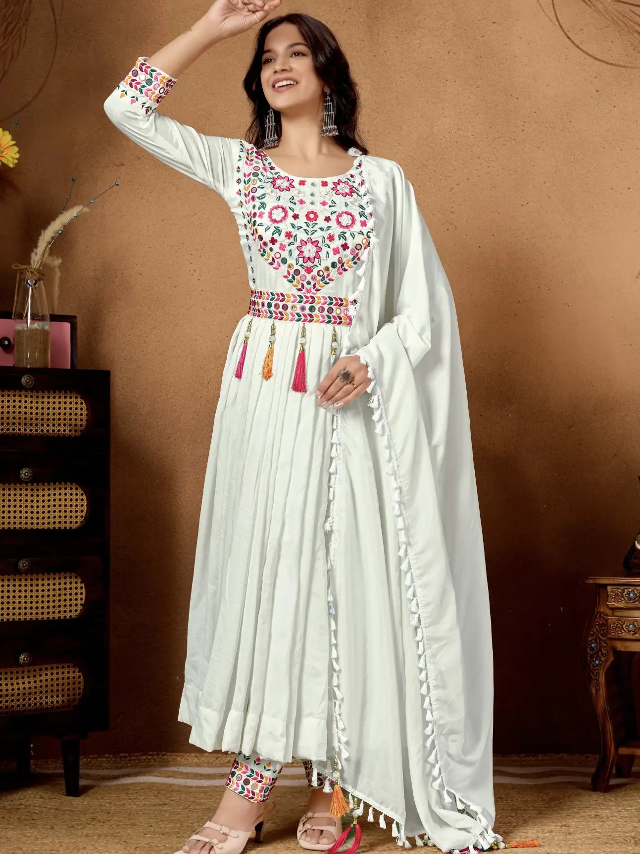 Woman wearing a white embroidered anarkali suit with a brown background