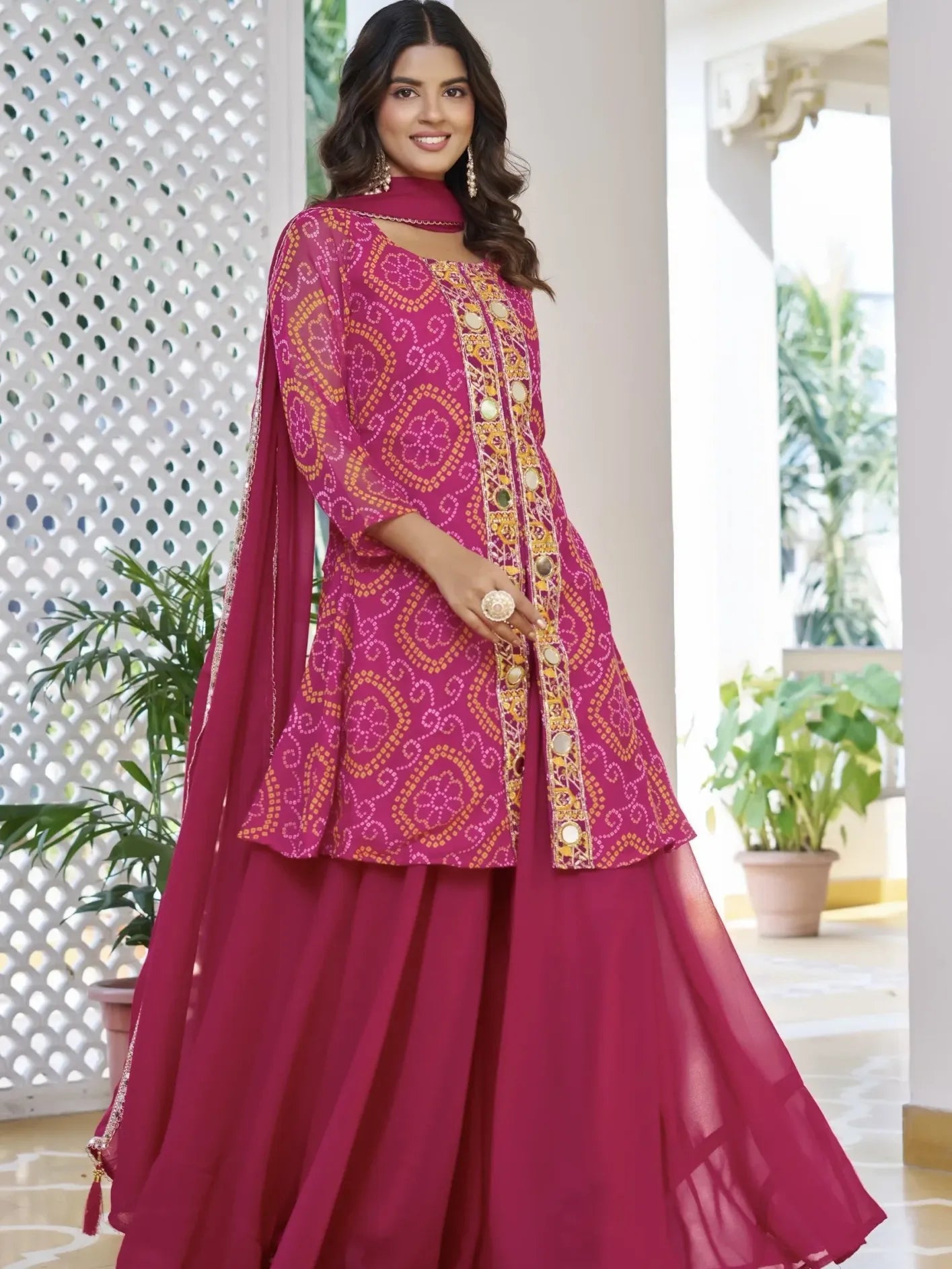 Woman wearing a pink traditional outfit with intricate patterns in an outdoor setting.