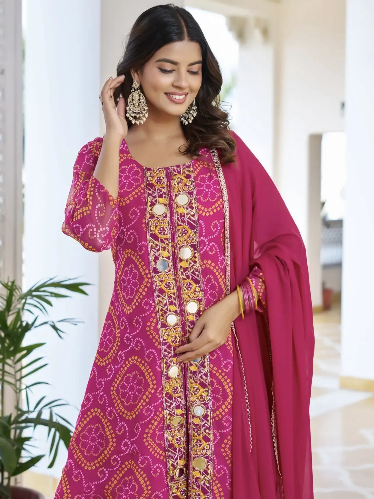 Woman wearing a pink embroidered traditional outfit with a matching dupatta indoors.