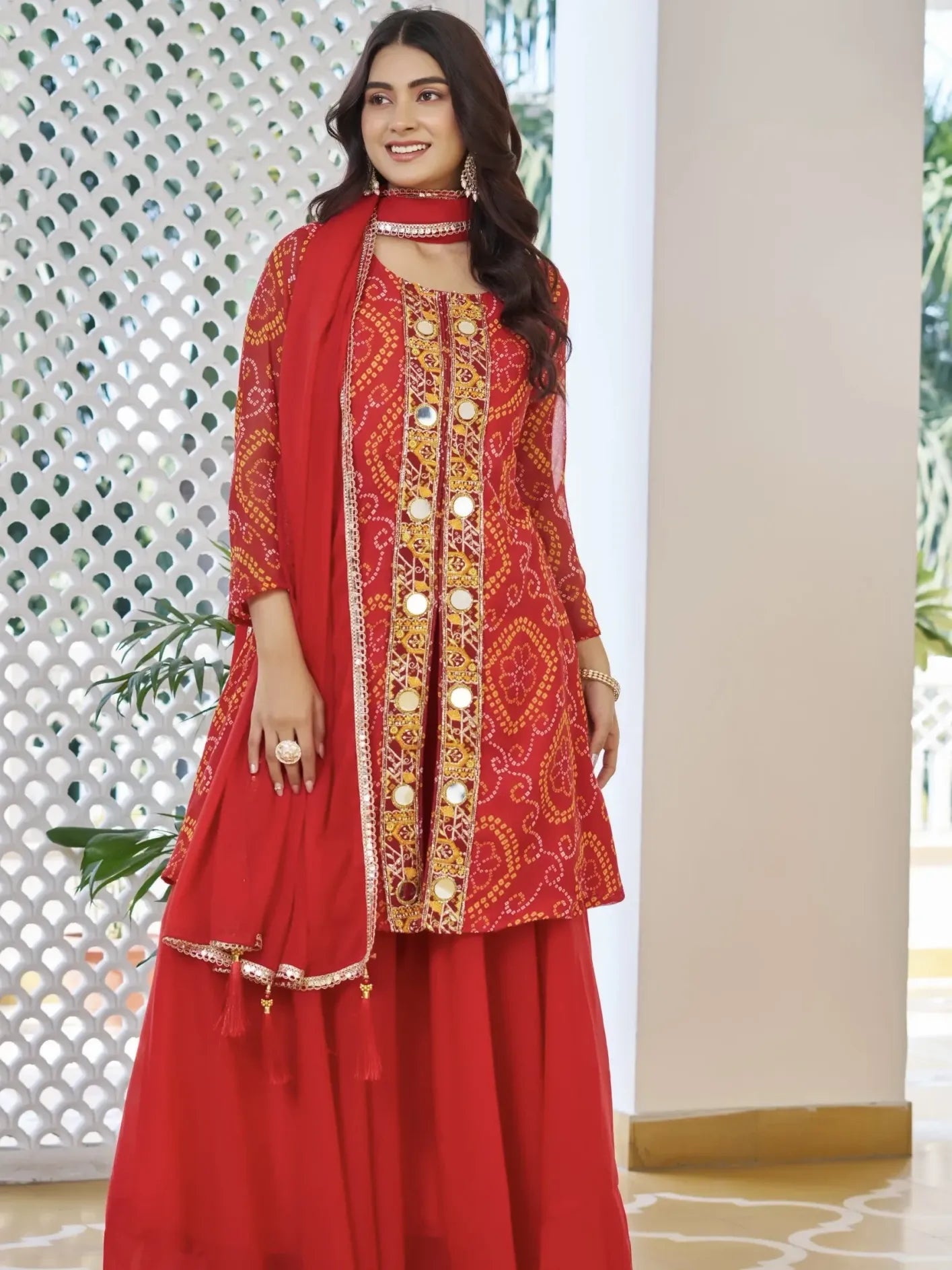Woman wearing a red traditional outfit with intricate gold embroidery in an indoor setting.