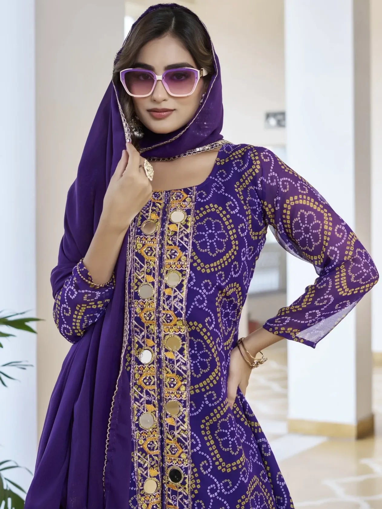 Woman wearing a purple embroidered dress and headscarf indoors.