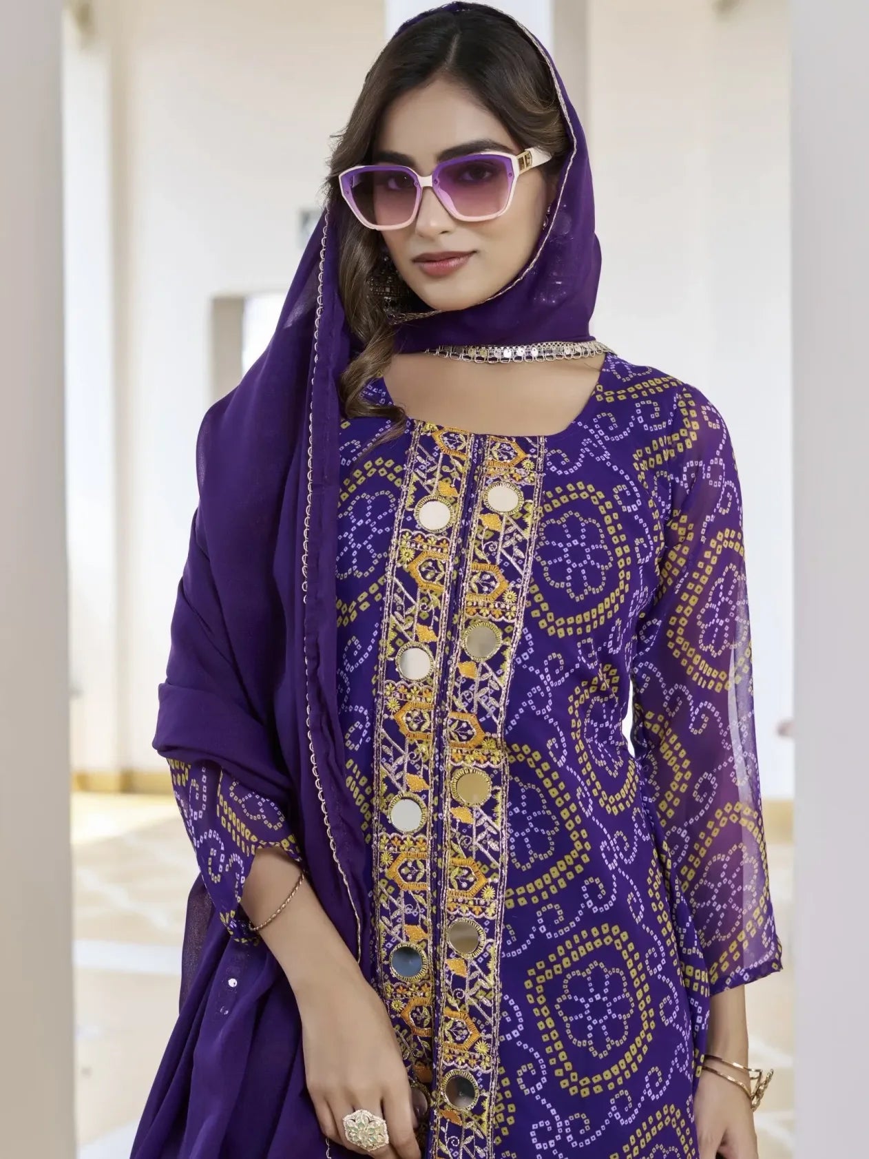 Woman wearing a purple embroidered outfit with sunglasses indoors
