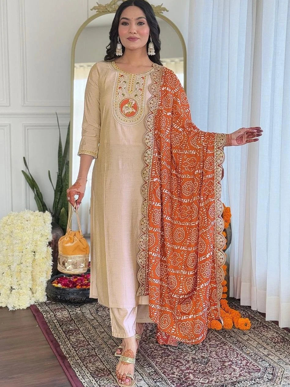 Woman in traditional outfit with beige kurta and orange dupatta in a decorated room.