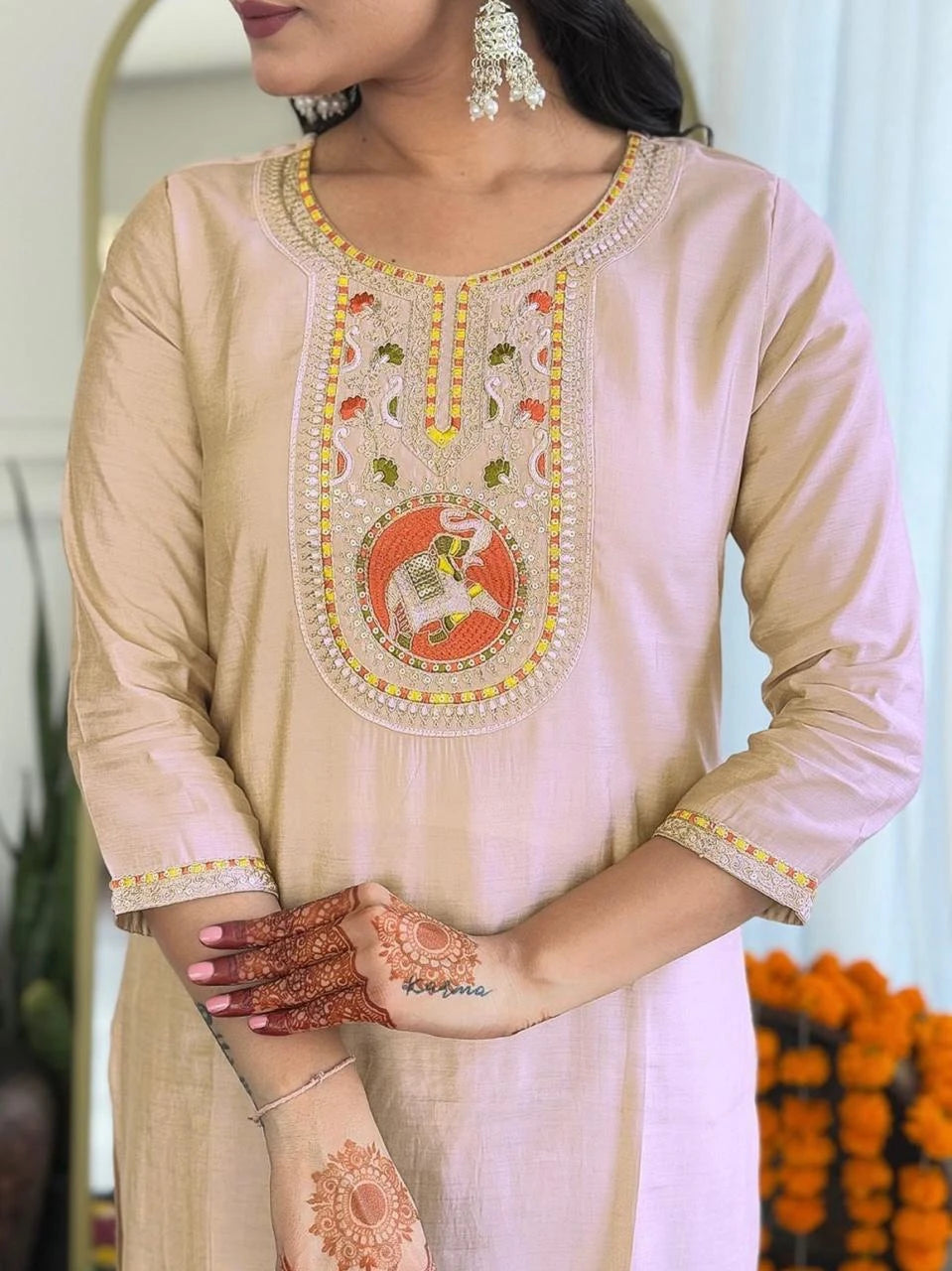 Beige embroidered kurta with intricate designs, worn by a person with henna on hands.