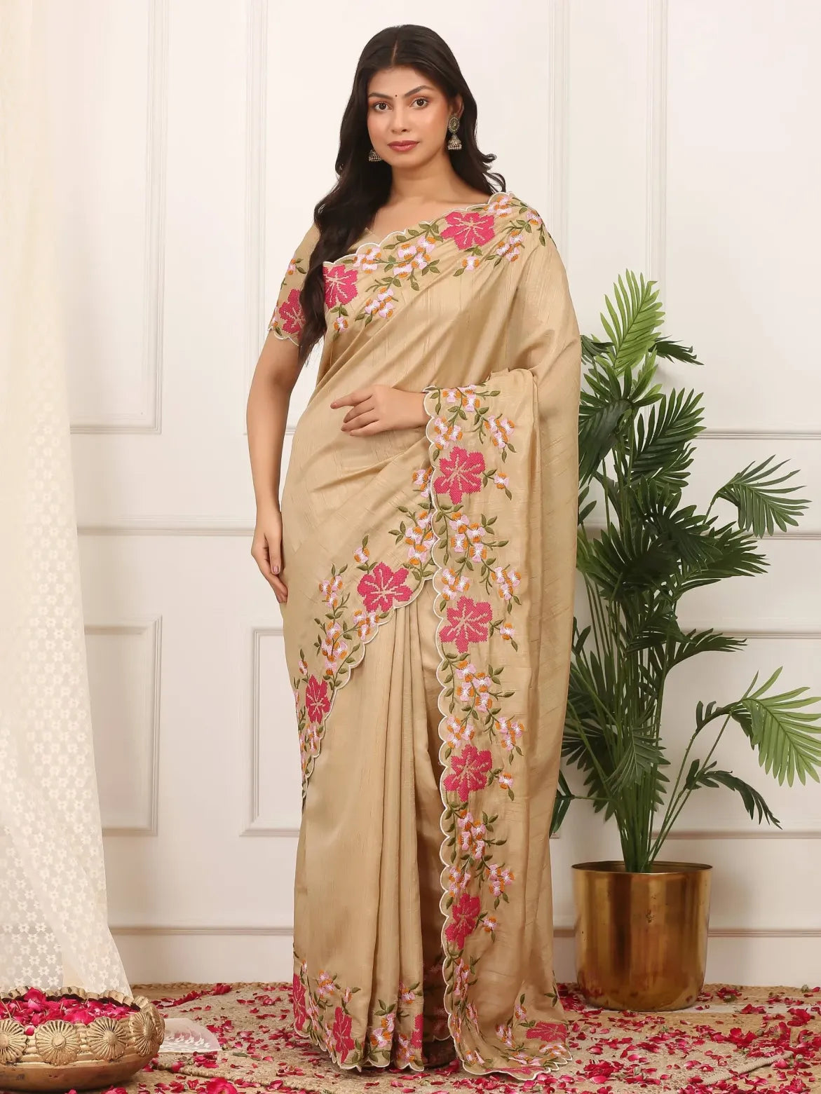 Woman wearing a beige saree with floral patterns in a decorated room.