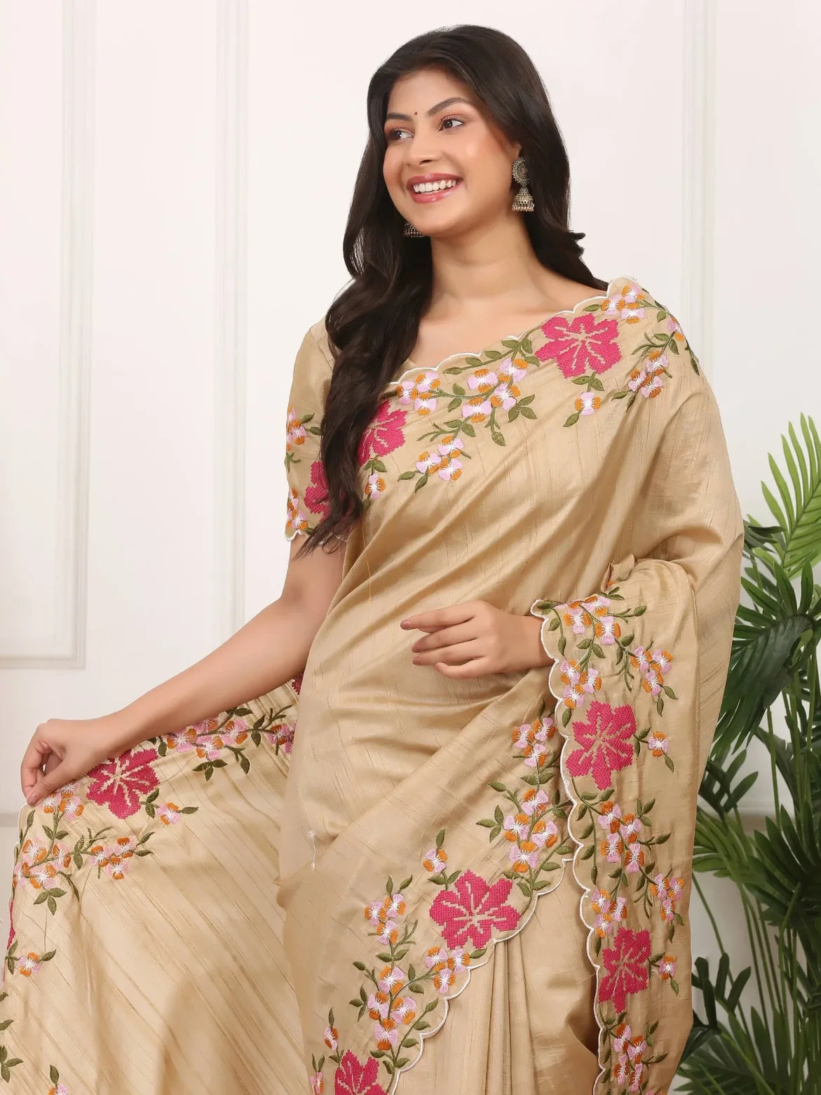 Woman wearing a beige saree with floral embroidery sitting indoors.