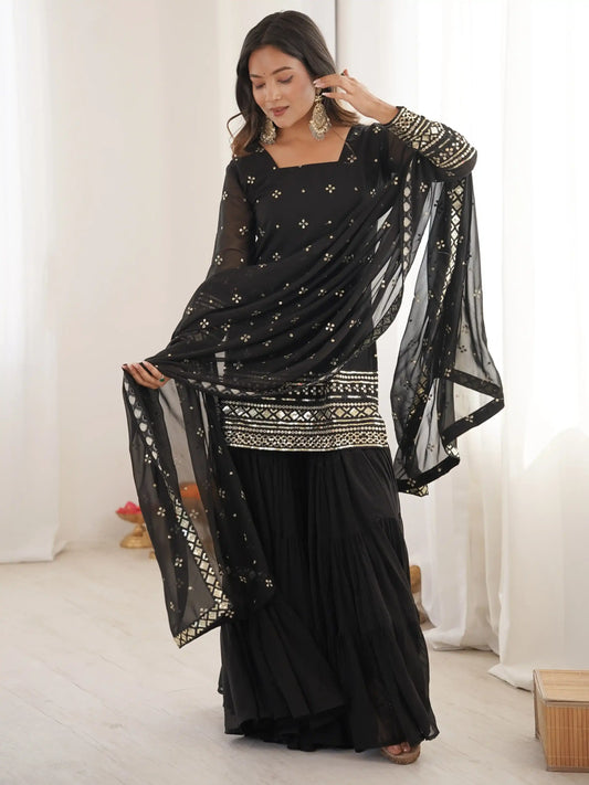 Woman wearing a black saree with gold patterns in a minimal indoor setting