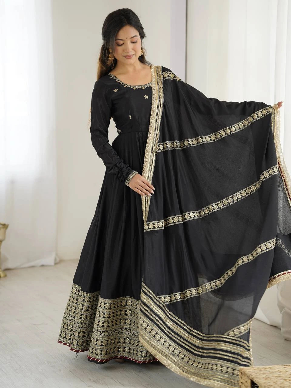 Woman wearing a black traditional outfit with a sheer dupatta in a well-lit room.