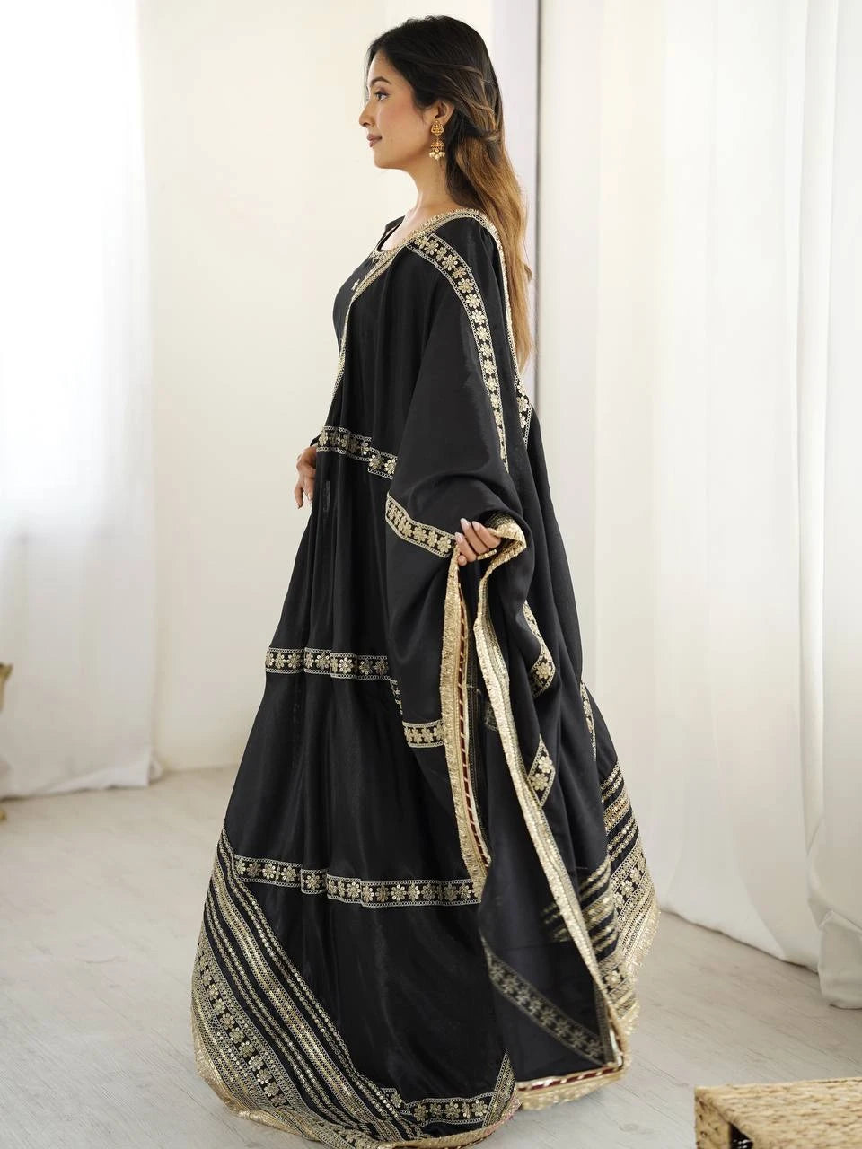 Woman wearing a black traditional outfit with gold embroidery in a minimal indoor setting