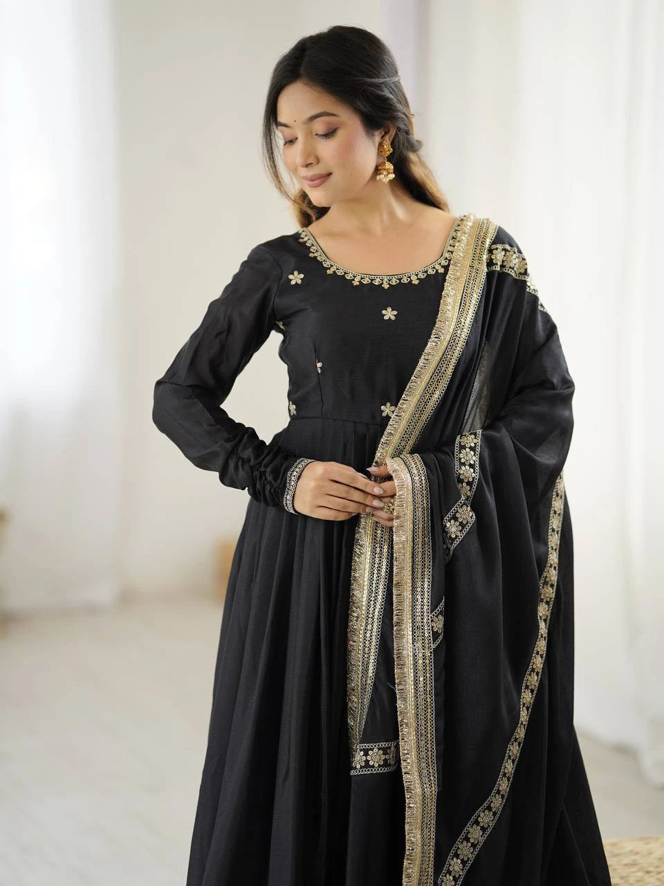 Woman wearing a black traditional outfit with gold embroidery in a softly lit room.