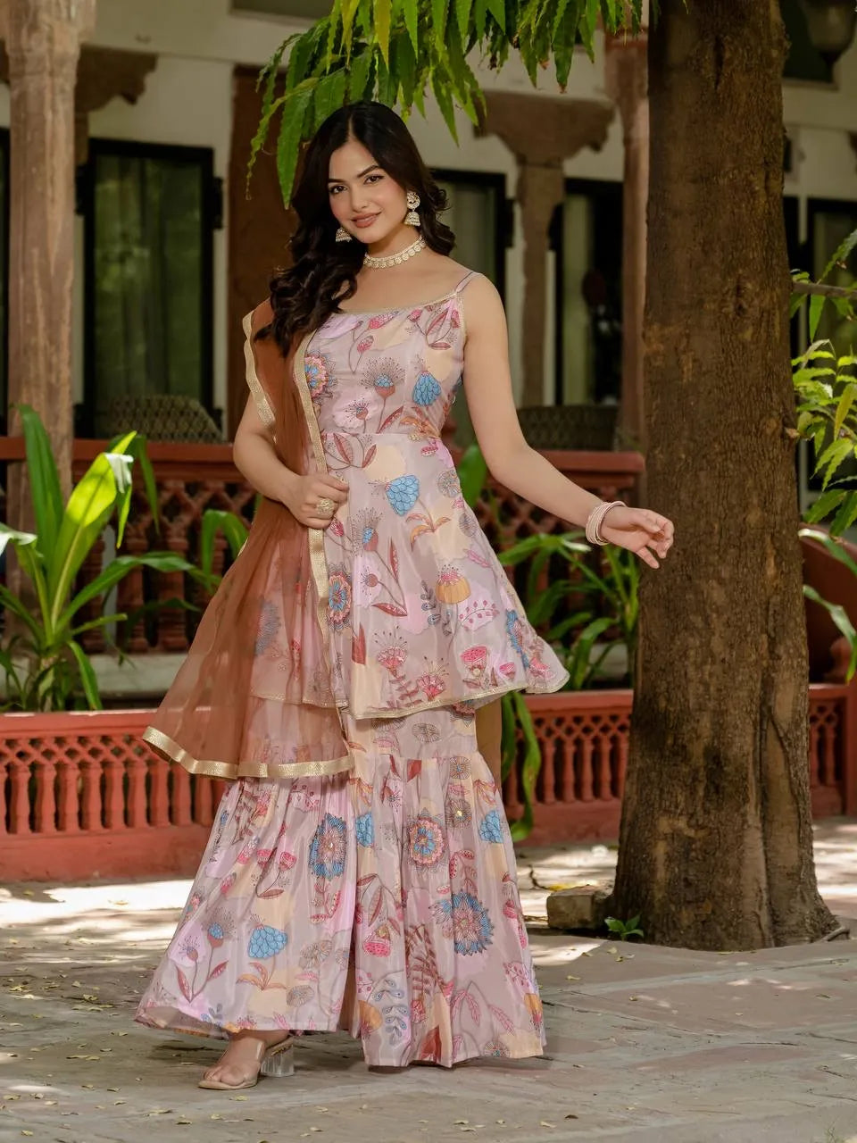 Woman in a floral dress standing outdoors with plants and a tree in the background