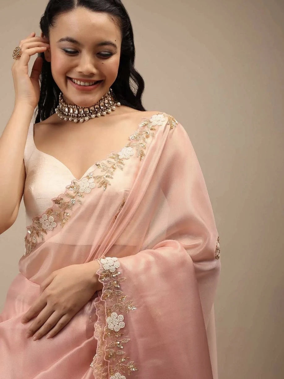 Woman wearing a pink saree with floral embroidery against a neutral background