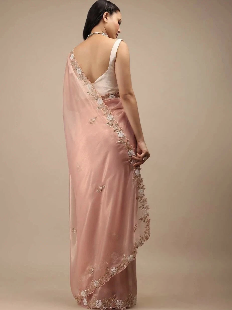 Woman wearing a pink saree with floral embroidery on a beige background