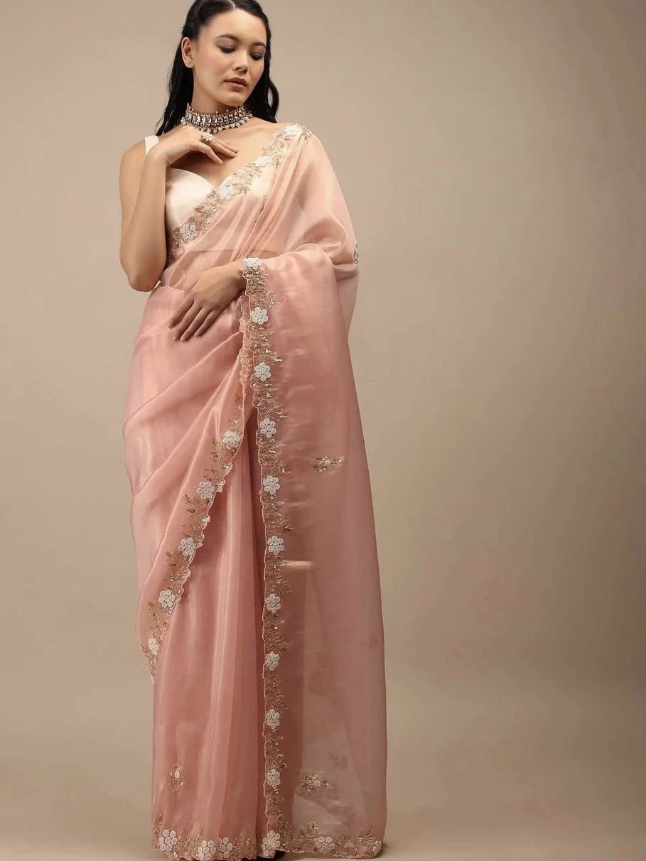 Woman wearing a pink saree with floral embroidery on a beige background