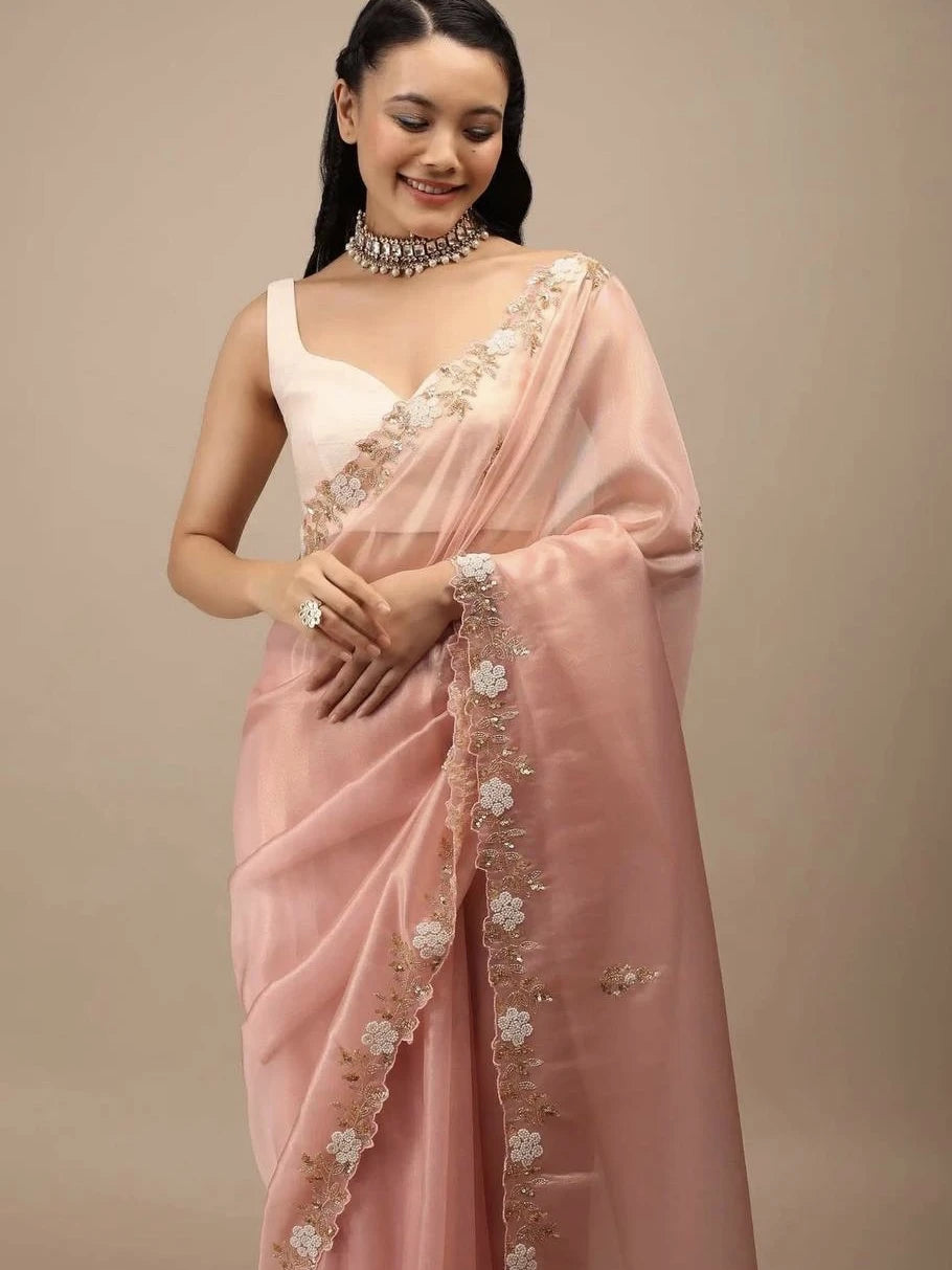 Woman wearing a pink saree with white floral embroidery on a beige background