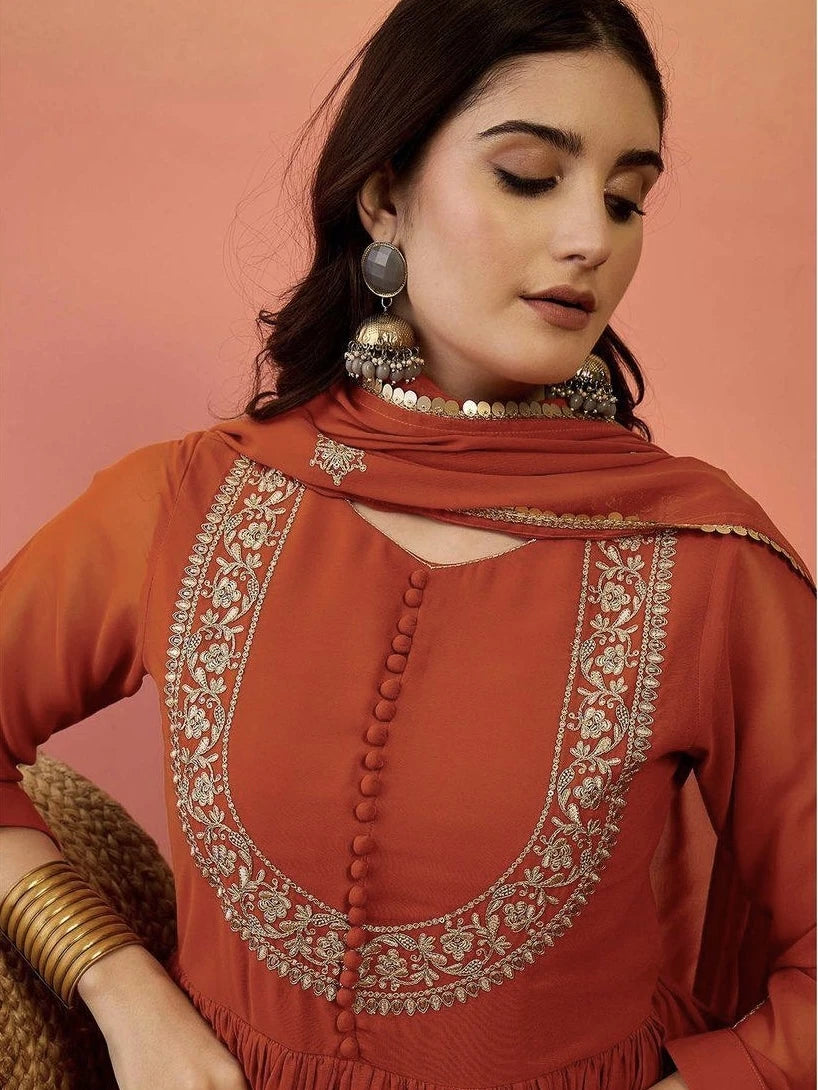 Woman wearing a rust-colored embroidered top with a plain background