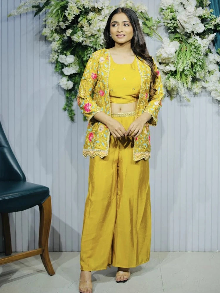 Woman in a yellow traditional outfit with floral embellishments standing in front of floral decorations.