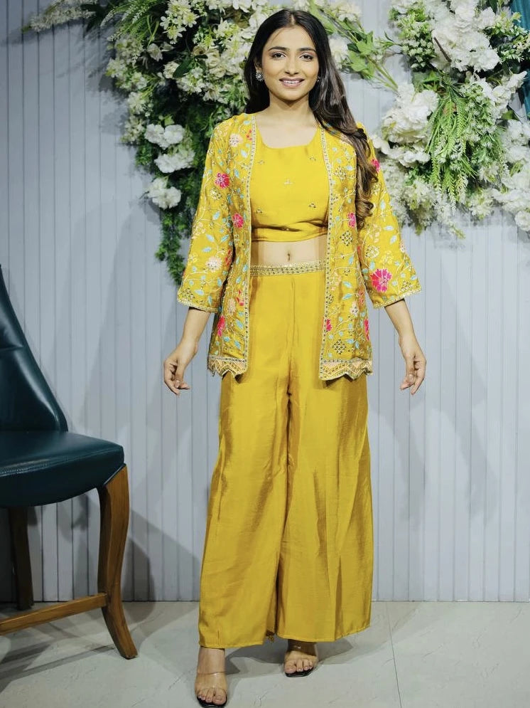 Woman in a yellow traditional outfit with floral patterns standing in front of floral decorations.
