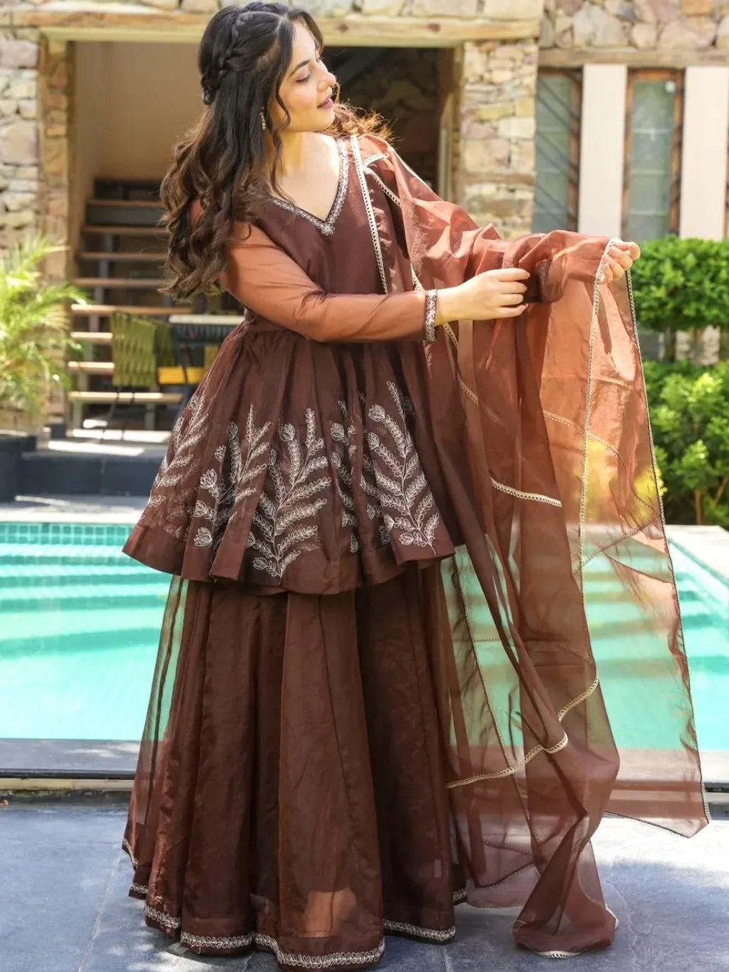 Woman in a brown traditional outfit standing by a poolside.