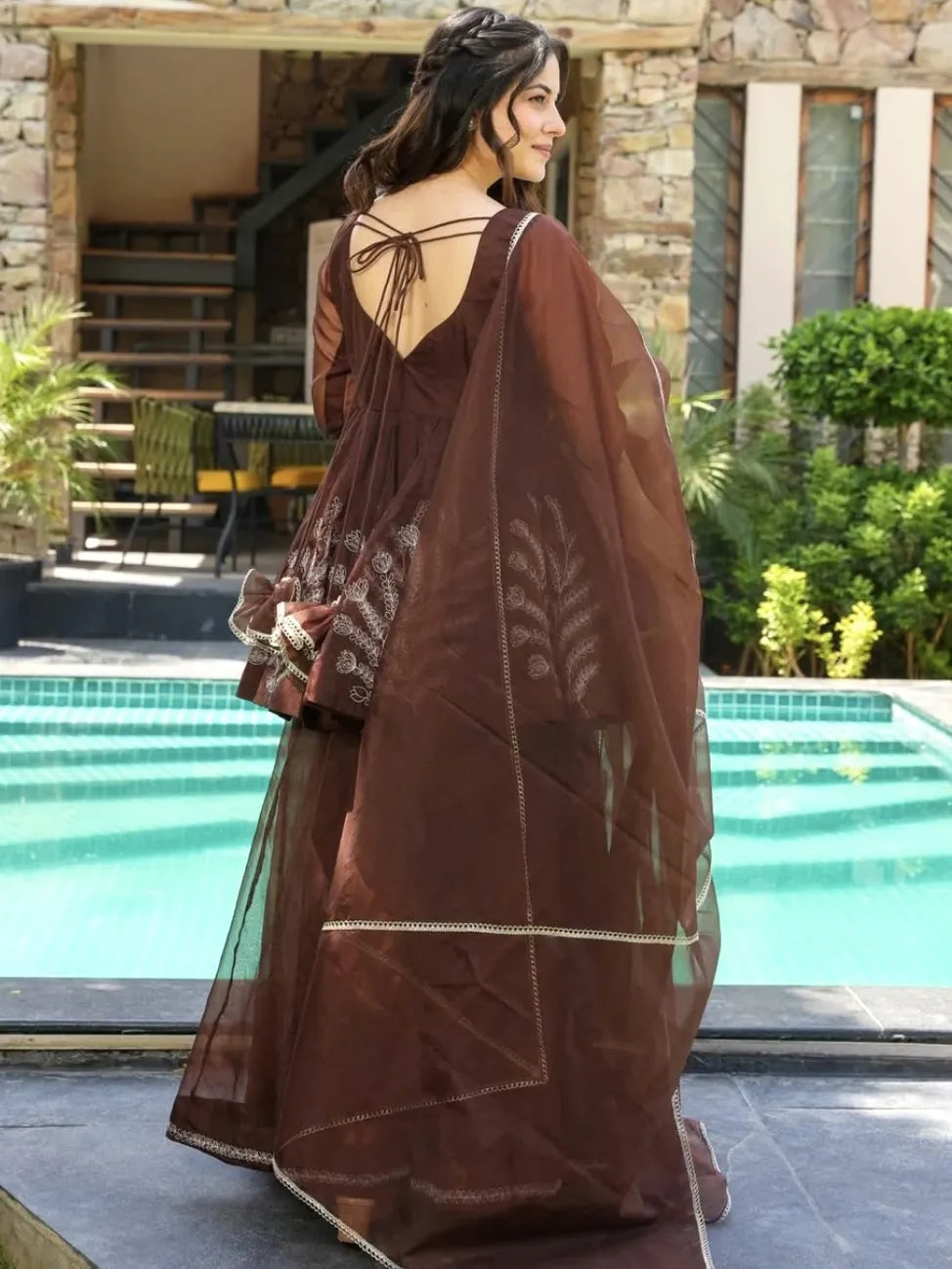 Woman in a brown sarara set standing by a poolside