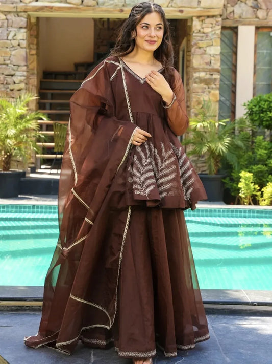 Woman in a brown traditional outfit standing by a pool with greenery in the background