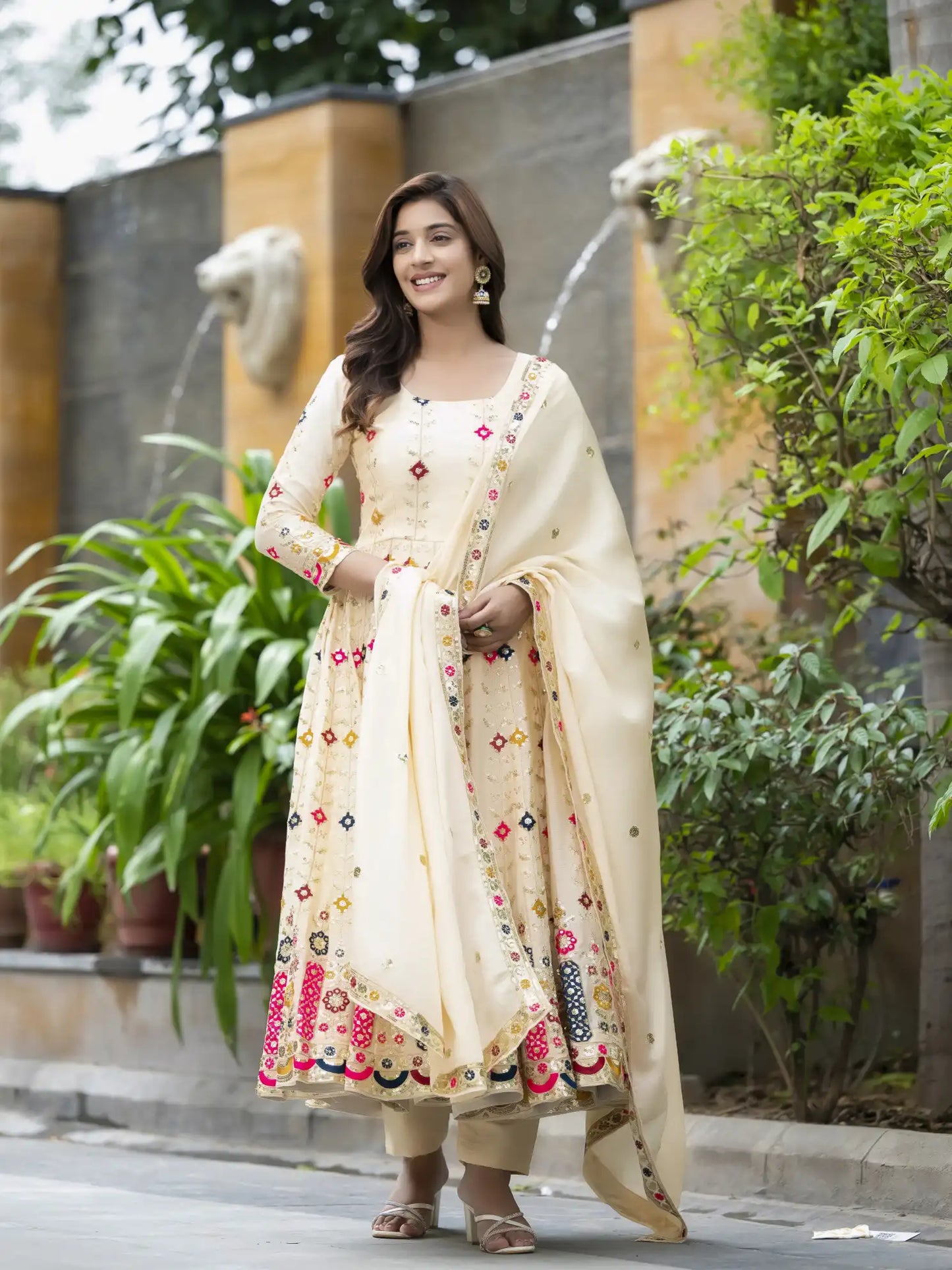 Woman in a cream-colored traditional outfit with floral patterns standing outdoors.