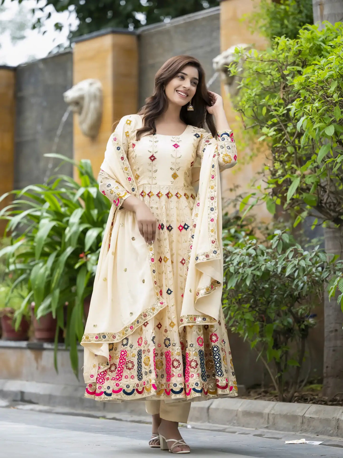 Woman in a cream-colored traditional outfit with floral patterns standing outdoors.