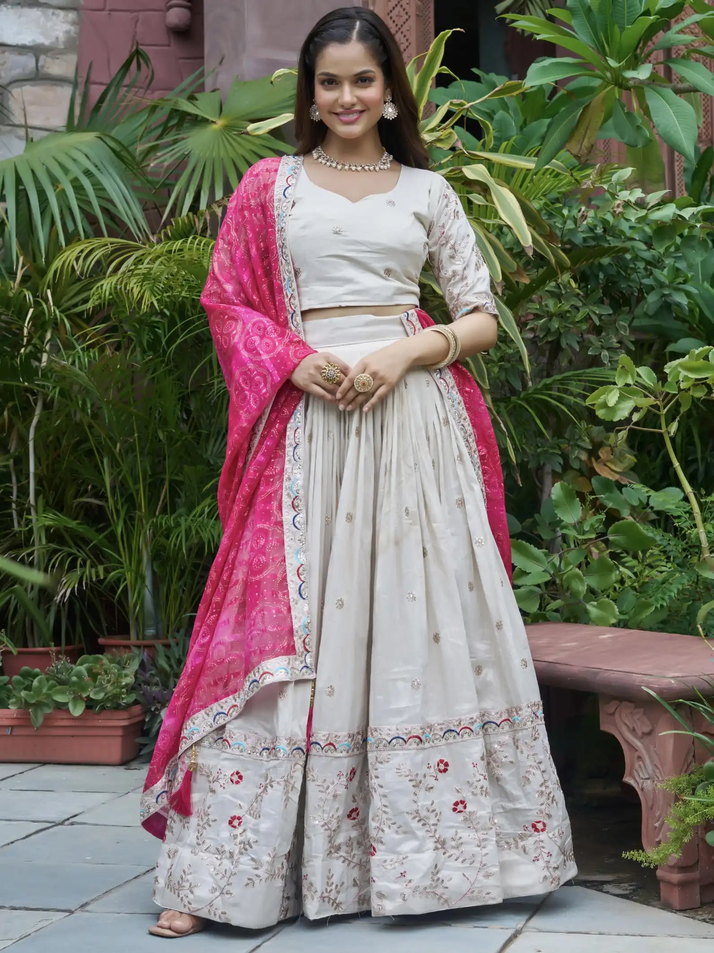 Woman in a white traditional outfit with pink dupatta standing in a garden.