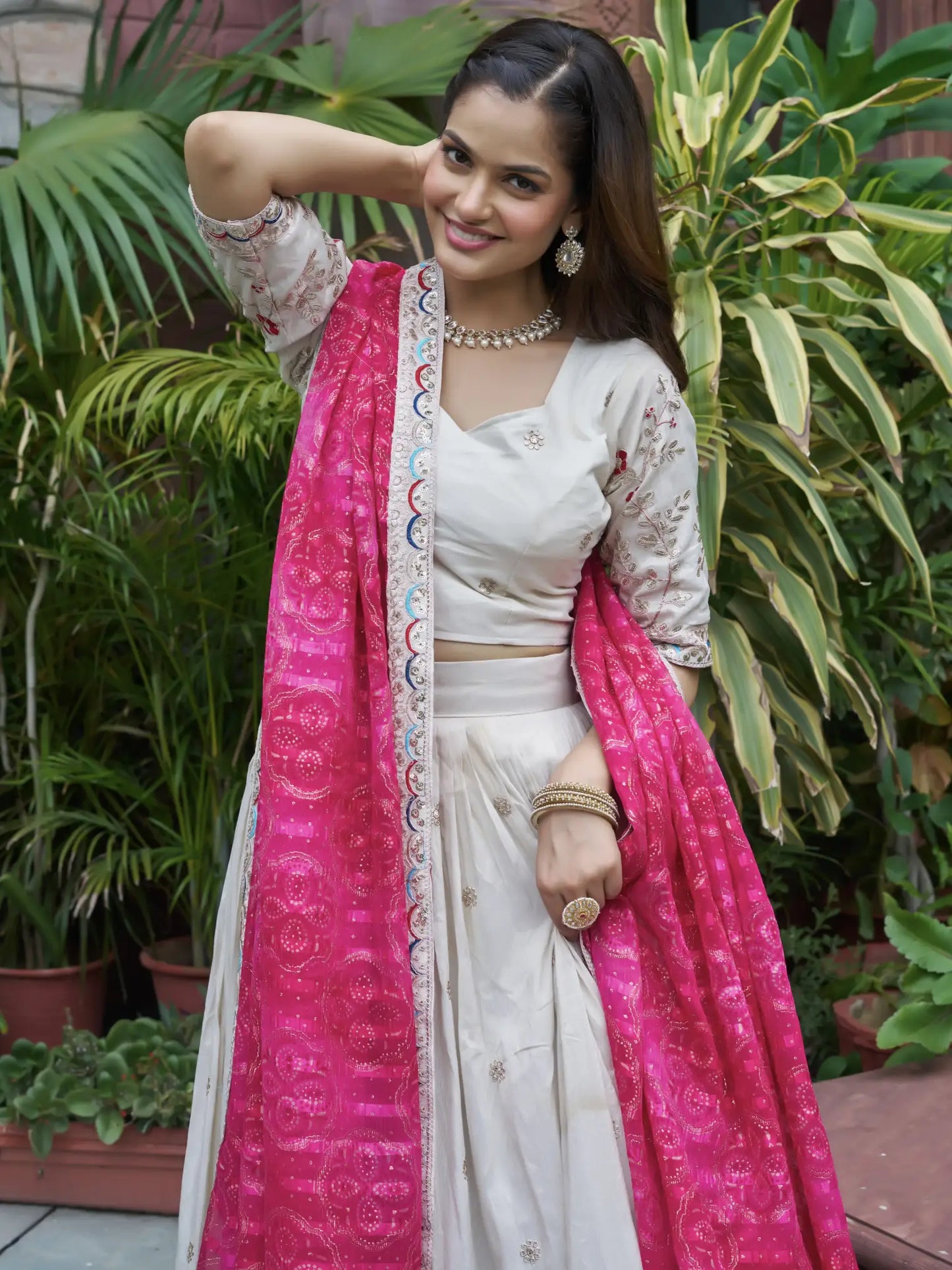 Woman in a white saree with pink dupatta standing in front of green plants