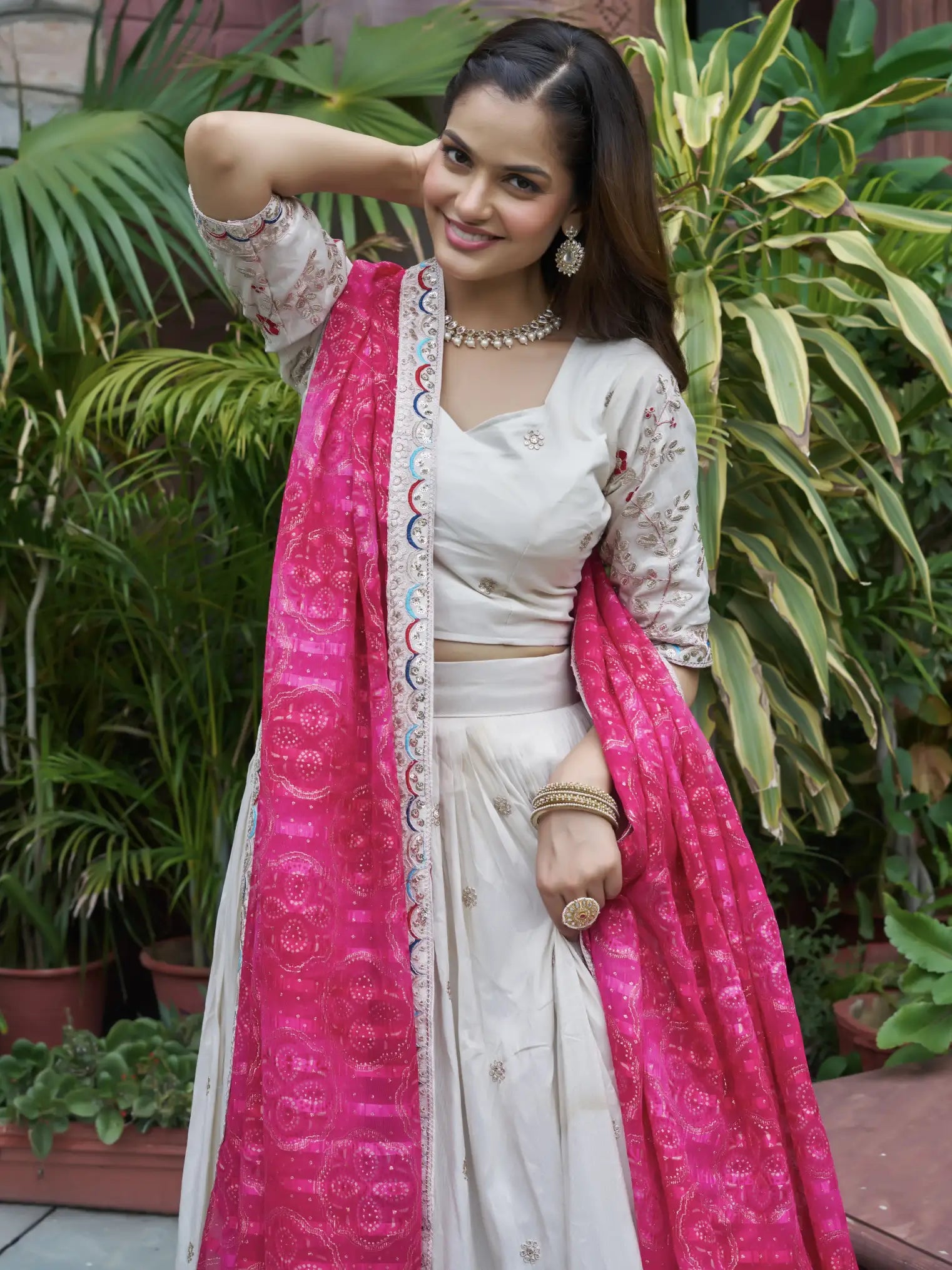 Woman in a white saree with pink dupatta standing in front of green plants