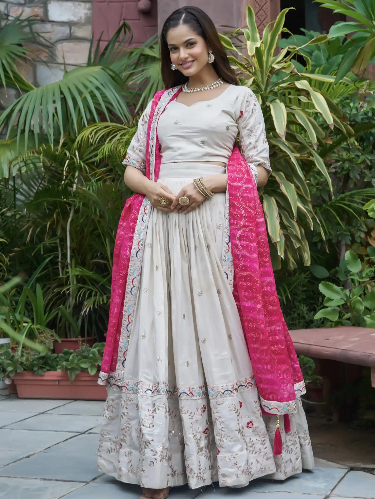 Woman in a traditional outfit with a pink dupatta standing outdoors.