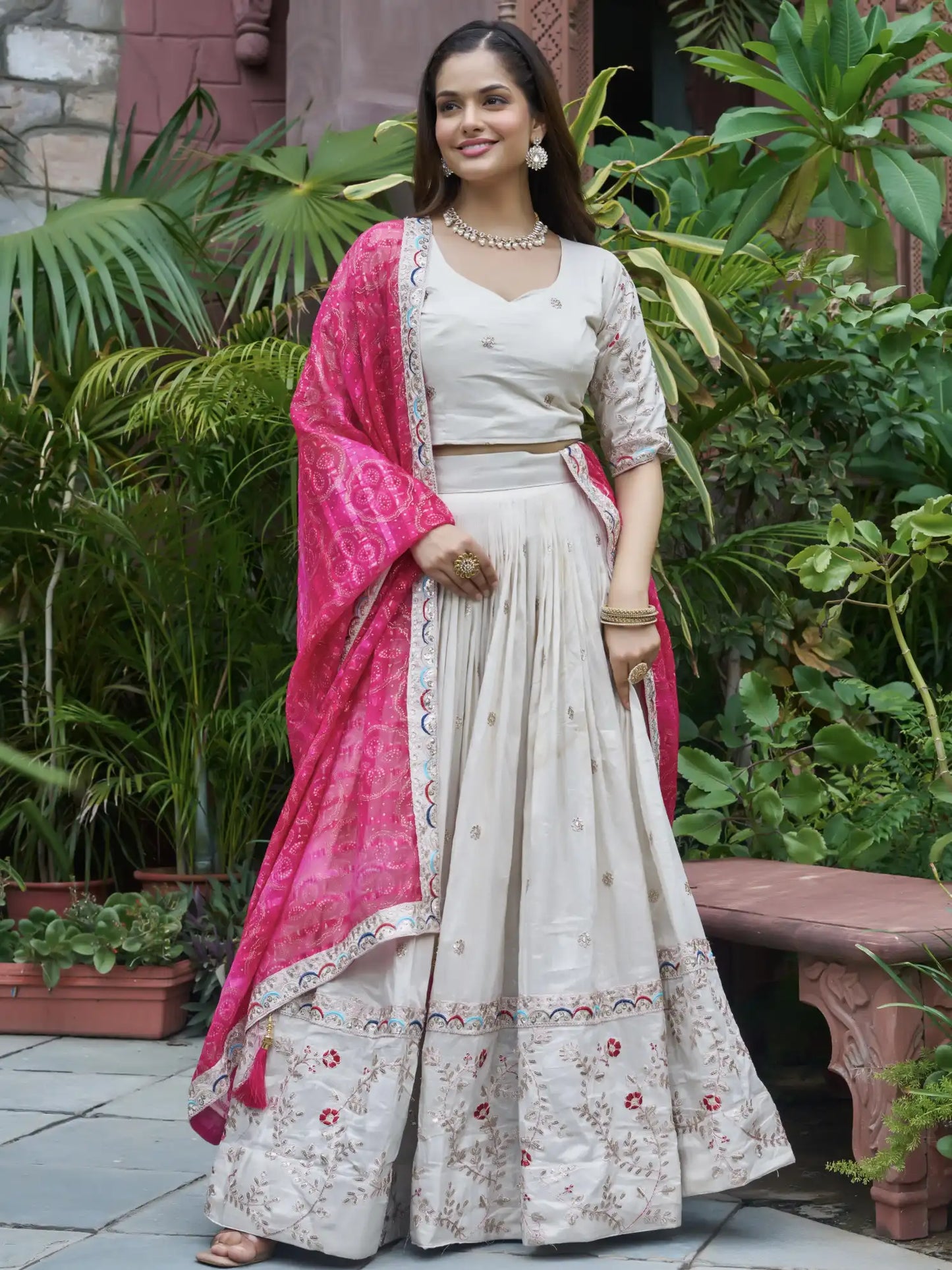 Woman in a traditional outfit with a pink dupatta standing in a garden.