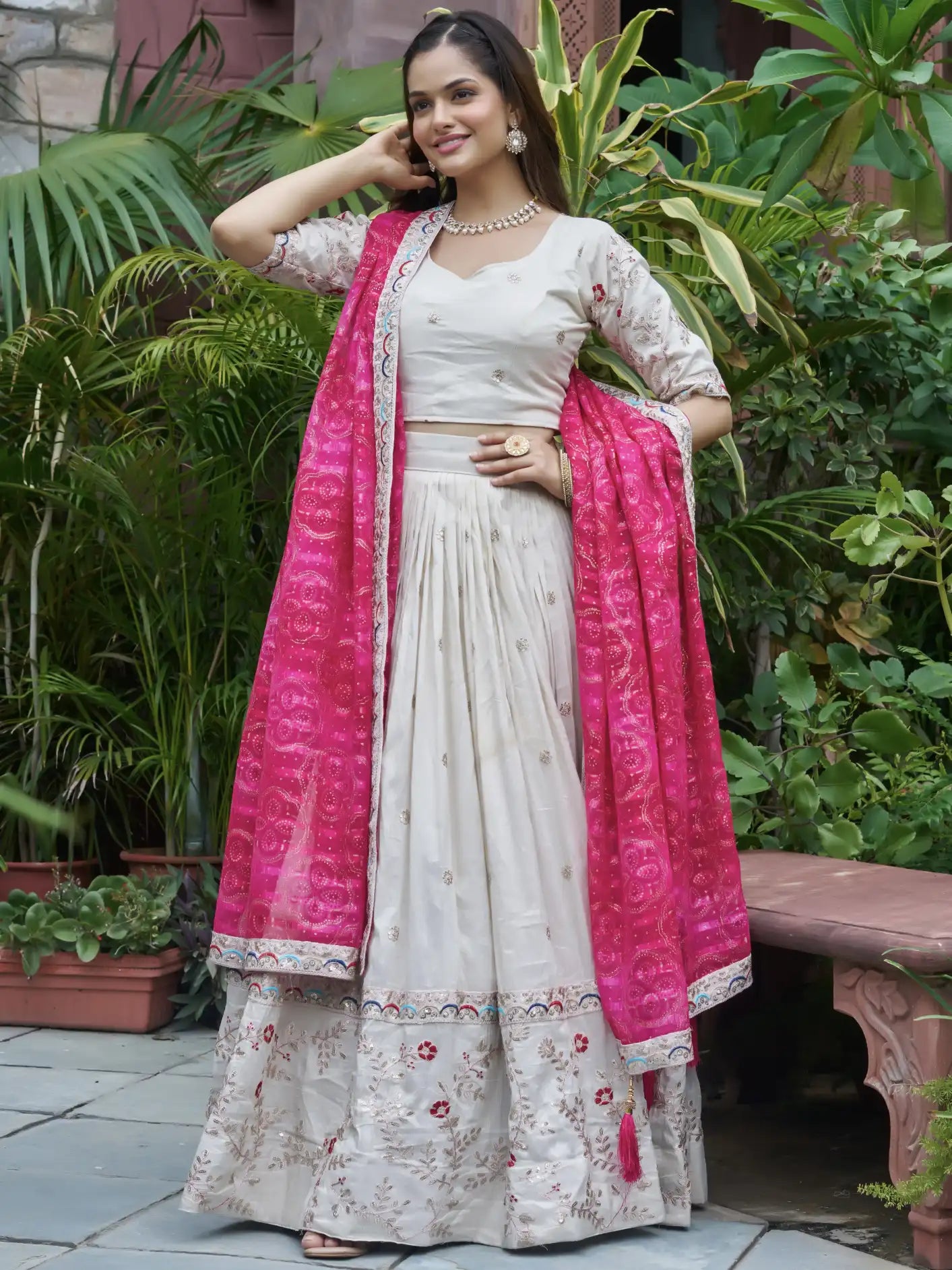 Woman in traditional outfit with pink dupatta standing outdoors among plants