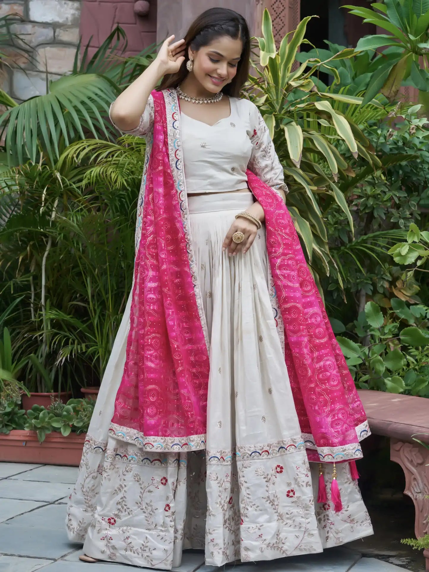 Woman in traditional outfit with pink dupatta standing outdoors among greenery