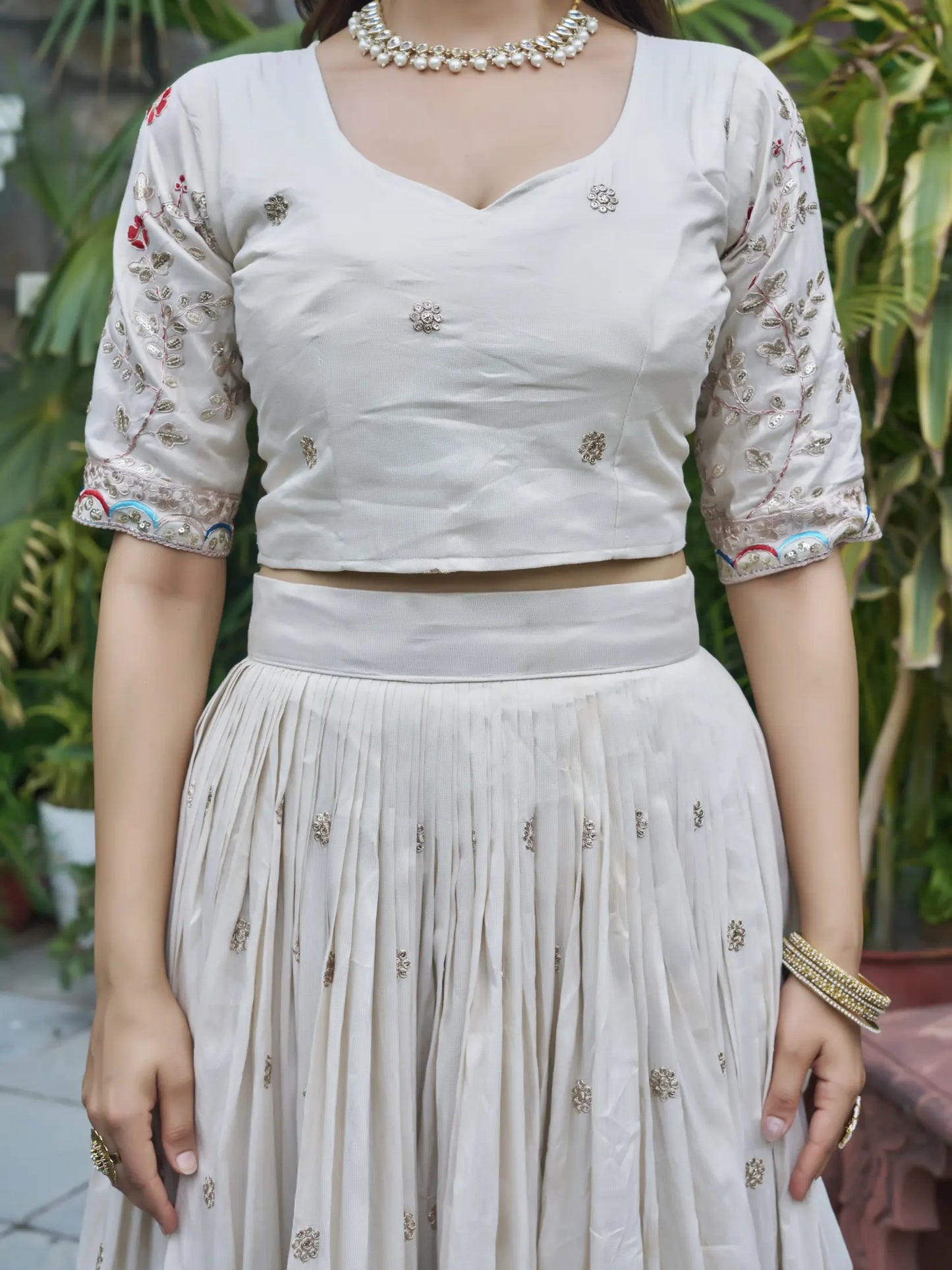 Person wearing a light-colored traditional outfit with embroidery, standing outdoors.